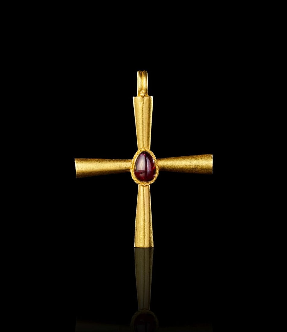 A BYZANTINE GOLD AND GARNET CROSS CIRCA 6TH CENTURY A.D.: A BYZANTINE GOLD AND GARNET CROSS CIRCA 6TH CENTURY A.D. Worked in gold and set with a central garnet, this Byzantine cross has a simple, balanced form with gently flaring arms and a plain suspension 