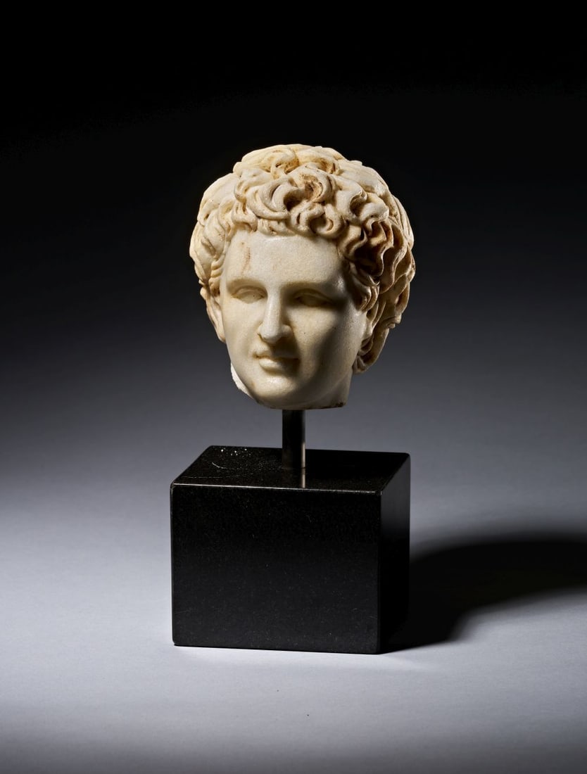 A ROMAN MARBLE HEAD OF A YOUNG MAN, CIRCA 1ST-2ND CENTURY A.D.: A ROMAN MARBLE HEAD OF A YOUNG MAN, CIRCA 1ST-2ND CENTURY A.D. Carved in marble, this Roman head of a young man is shown with a softly modelled face and a full mass of curling hair. The head is slight
