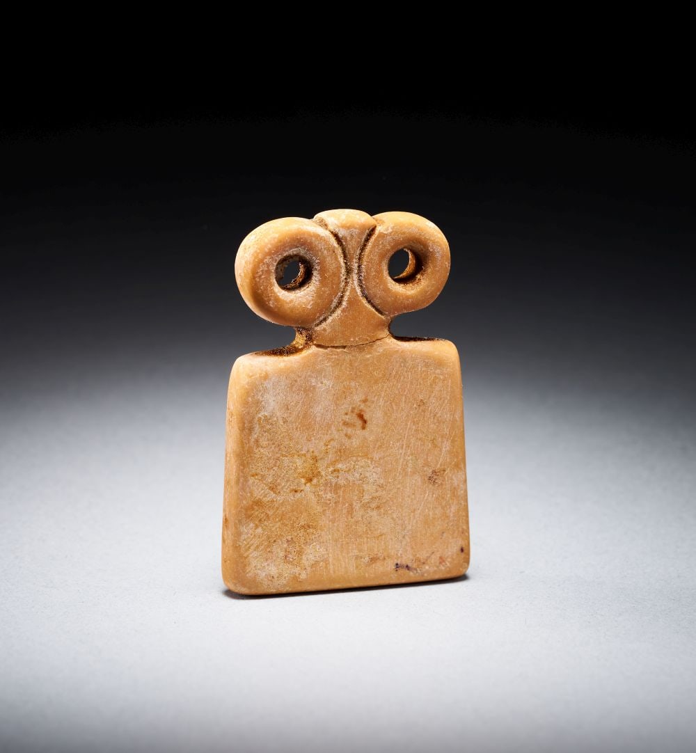 A MARBLE """"EYE"""" IDOL TELL BRAK REGION CIRCA 4TH MILLENNIUM B.C.: A MARBLE """"EYE"""" IDOL TELL BRAK REGION CIRCA 4TH MILLENNIUM B.C. A marble “eye” idol from the Tell Brak region, circa 4th millennium B.C., carved in a warm beige stone with a broad rec