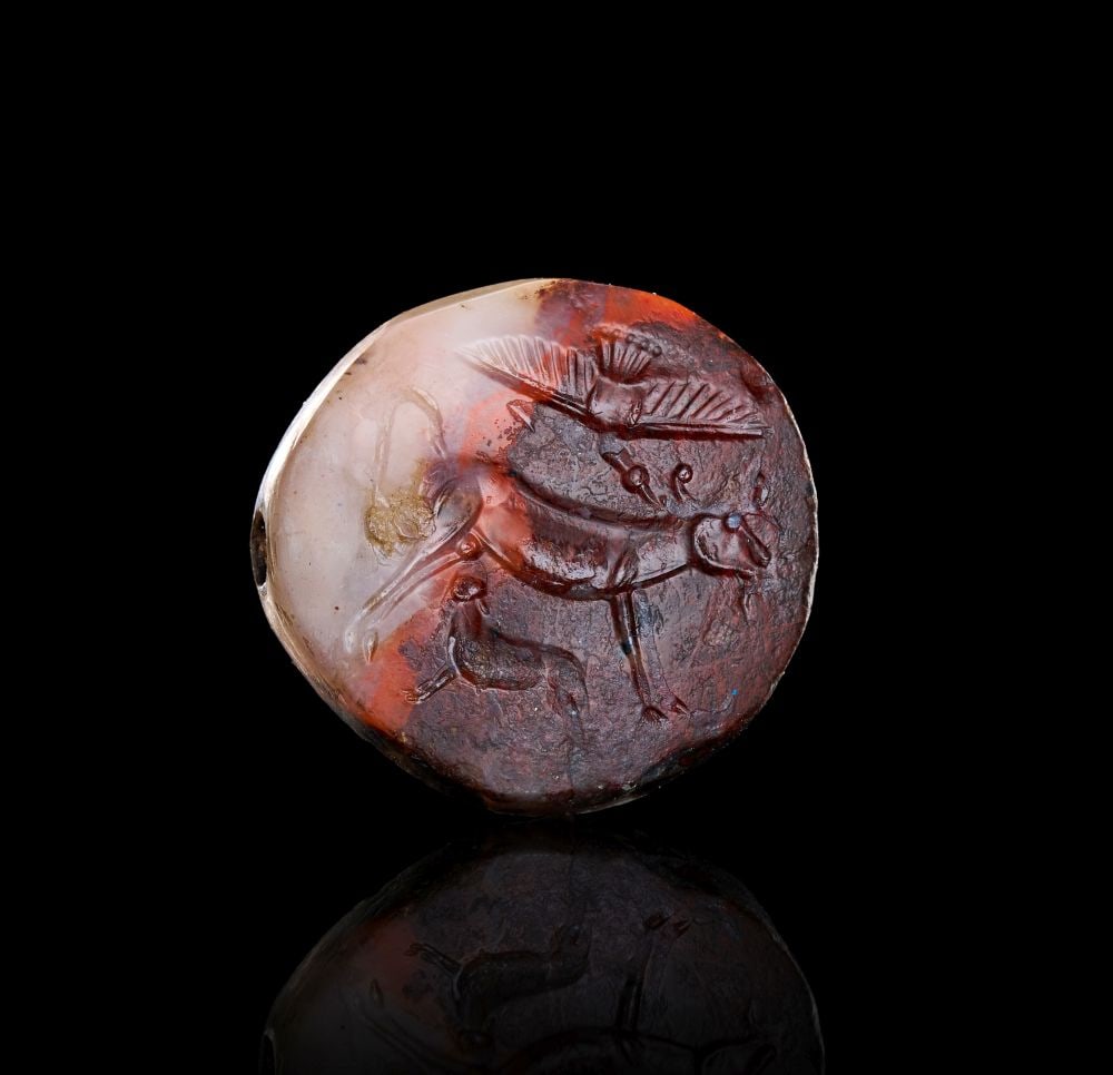 A FINELY ENGRAVED MINOAN LENTOID AGATE STAMP SEAL DEPICTING A SACRED BOVINE GROUP WITH BIRD, LATE MI: A FINELY ENGRAVED MINOAN LENTOID AGATE STAMP SEAL DEPICTING A SACRED BOVINE GROUP WITH BIRD, LATE MINOAN I-II, CIRCA 1600-1400 B.C. Of lentoid form, carved in mottled banded agate, the intaglio engrav