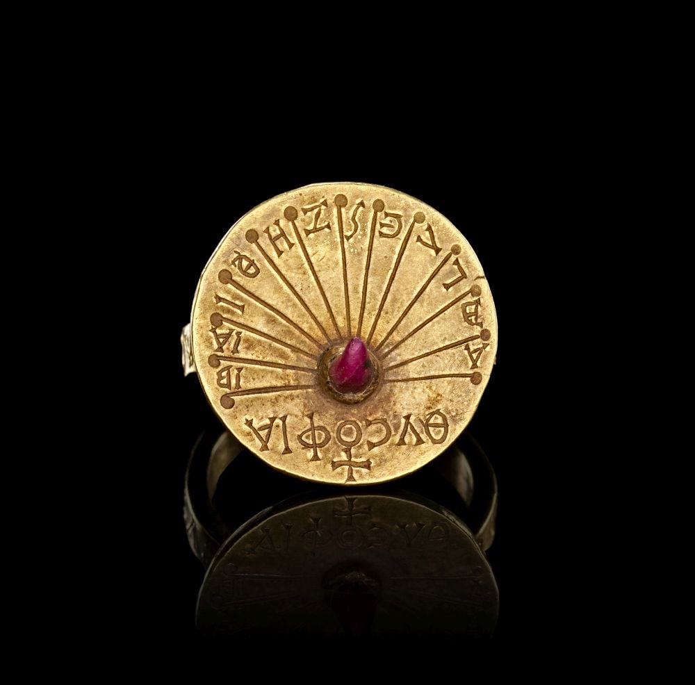 AN EXCEPTIONAL BYZNATINE GREEK INSCRIBED RING, CIRCA 7TH-9TH CENTURY A.D.: AN EXCEPTIONAL BYZNATINE GREEK INSCRIBED RING, CIRCA 7TH-9TH CENTURY A.D. This exceptional Byzantine Greek ring is formed in gold with a circular disc bezel set at the centre with a small pink stone. 