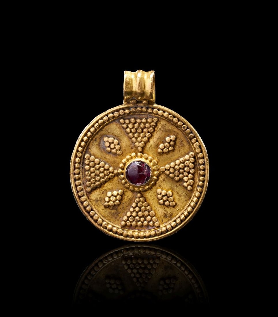 AN ANGLO-SAXON GOLD & GARNET PENDANT, CIRCA 6TH-7TH CENTURY A.D.: AN ANGLO-SAXON GOLD & GARNET PENDANT, CIRCA 6TH-7TH CENTURY A.D. An Anglo-Saxon gold pendant of circular form, centred with a cabochon garnet set within a raised gold collar. The face is richly de