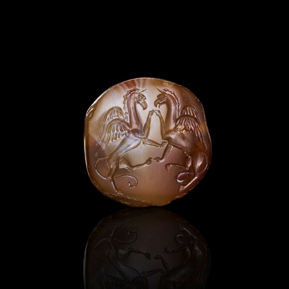 ARCHAIC EASTERN GREEK BANDED AGATE STAMP SEAL CIRCA 6th–5th CENTURY B.C.: ARCHAIC EASTERN GREEK BANDED AGATE STAMP SEAL CIRCA 6th–5th CENTURY B.C. Finely engraved stamp seal in translucent banded agate, depicting two confronted griffins rearing in heraldic symmetry, t