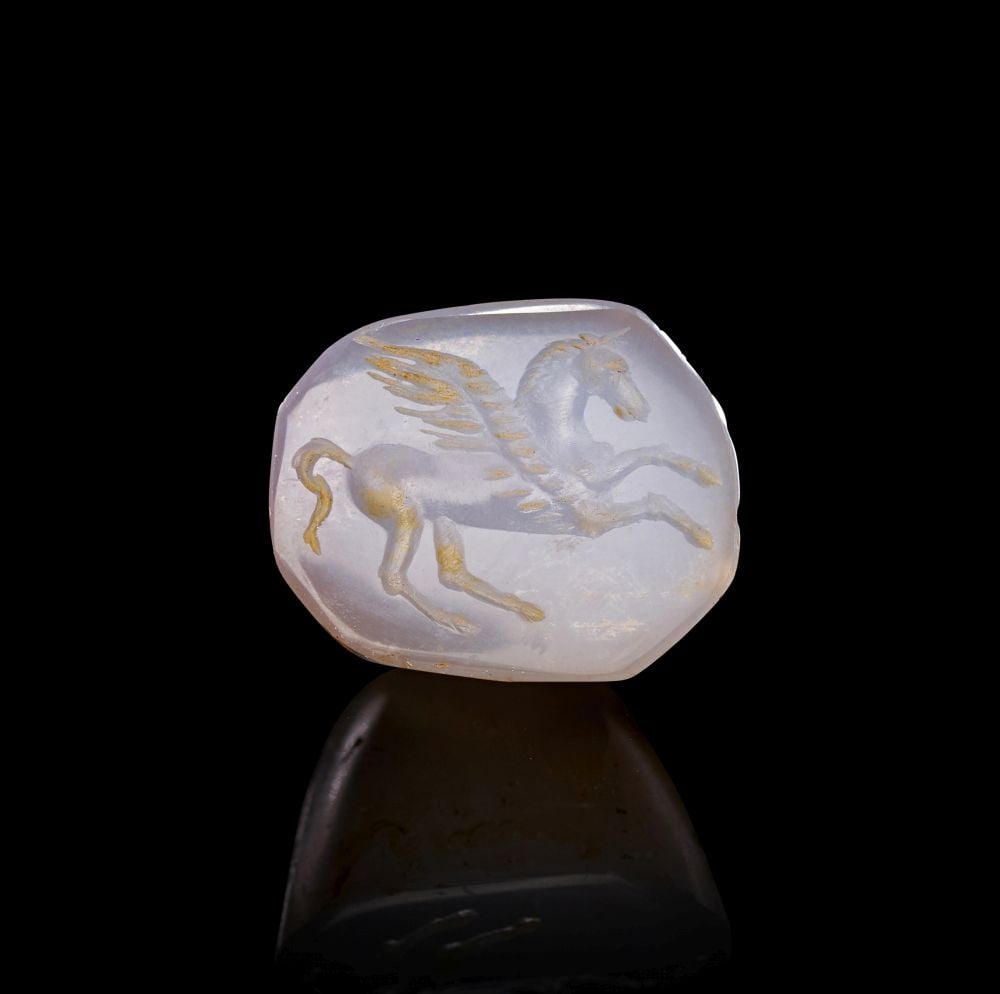A GRAECO-PERSIAN CHALCEDONY STAMP SEAL DEPICTING A UNICORN, WINGED FLYING HORE WITH A HORN ON ITS HE: A GRAECO-PERSIAN CHALCEDONY STAMP SEAL DEPICTING A UNICORN, WINGED FLYING HORE WITH A HORN ON ITS HEAD A Graeco-Persian chalcedony stamp seal, carved from translucent pale grey-white stone with soft p