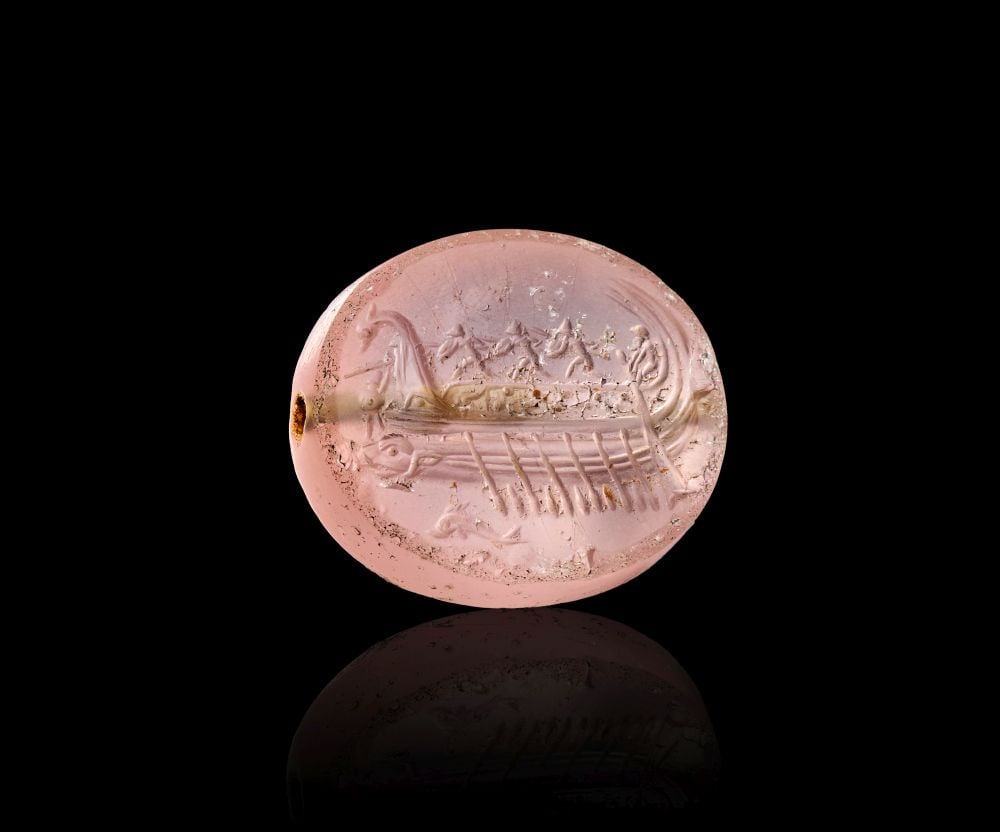 A GREEK GLASS SCARABOID WITH PROTESILAOS & SEA CREATURES, CLASSICAL PERIOD, CIRCA 4TH CENTURY B.C.: A GREEK GLASS SCARABOID WITH PROTESILAOS & SEA CREATURES, CLASSICAL PERIOD, CIRCA 4TH CENTURY B.C. A Greek glass scaraboid of translucent pale pink hue, pierced longitudinally for suspension. The 