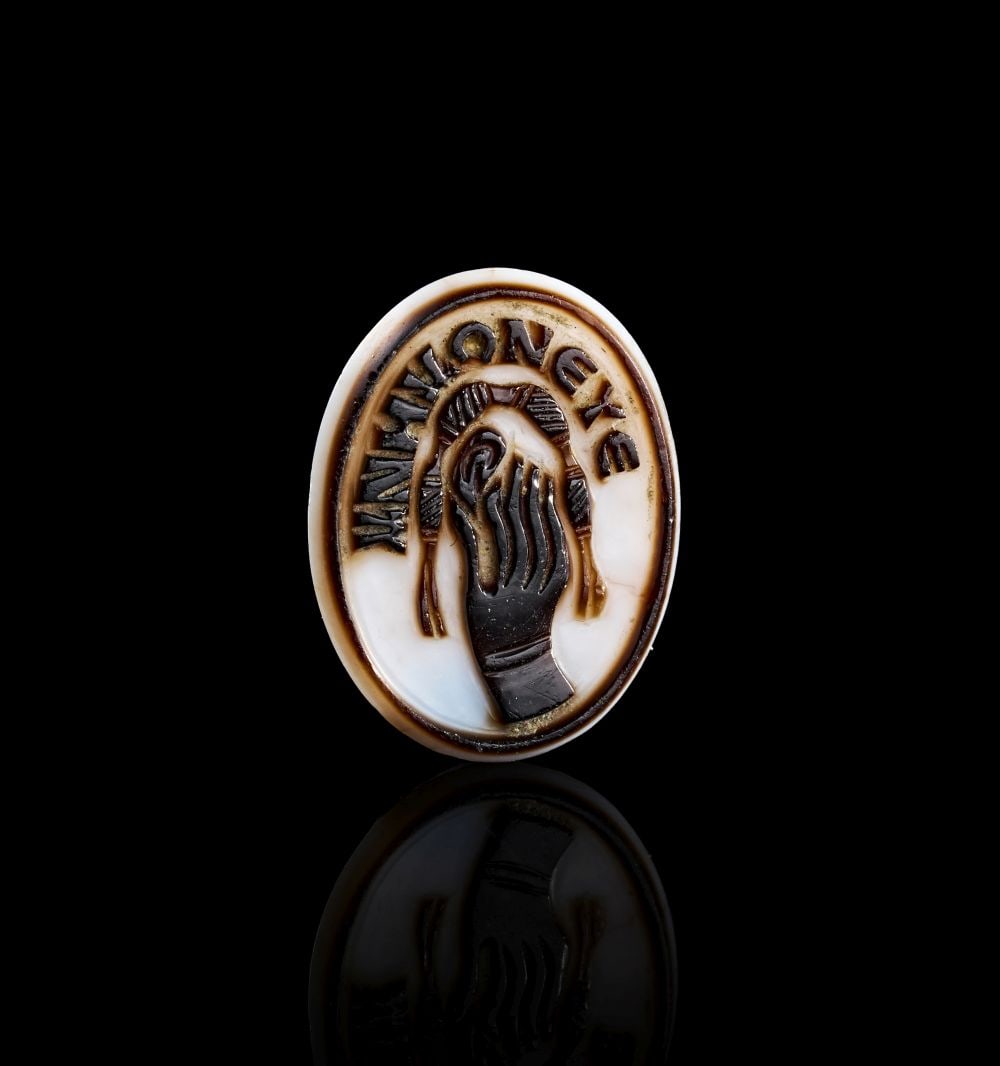 A ROMAN AGATE ""REMEBER ME"" CAMEO CIRCA 3RD-5TH CENTURY A.D.: A ROMAN AGATE ""REMEBER ME"" CAMEO CIRCA 3RD-5TH CENTURY A.D. A Roman agate cameo of oval form, carved in contrasting layers of dark brown and white stone. The central device depicts a right hand, sho
