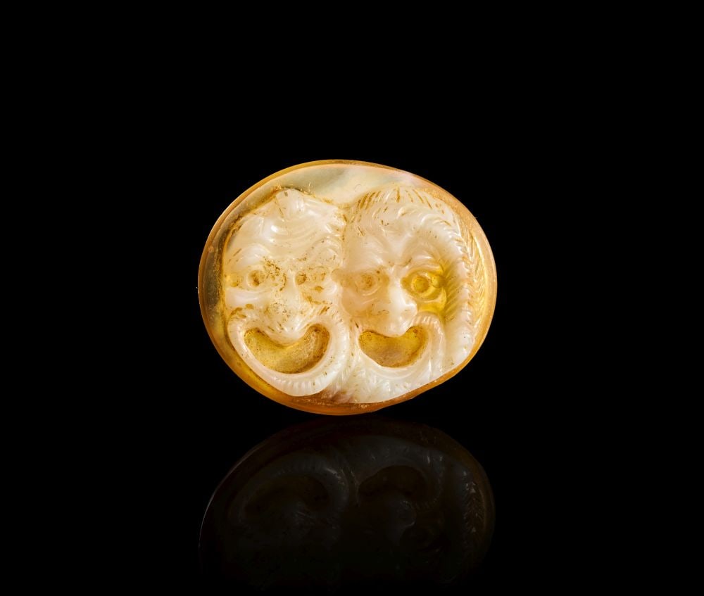 AN UNUSUAL ROMAN CAMEO OF A CONJOINED THEATRICAL MASK, CIRCA 1ST CENTURY A.D.: AN UNUSUAL ROMAN CAMEO OF A CONJOINED THEATRICAL MASK, CIRCA 1ST CENTURY A.D. An unusual Roman cameo carved as a conjoined theatrical mask, worked in a warm golden-yellow and creamy white banded stone
