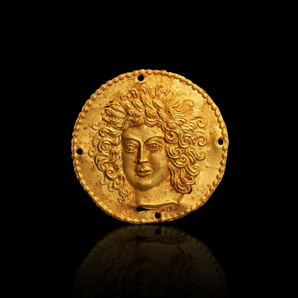 AN ELABORATE HELLENISTIC HIGH KARAT GOLD APPLIQUE OF A FEMALE GODDESS (MEDUSA), CIRCA 2ND CENTURY B.: AN ELABORATE HELLENISTIC HIGH KARAT GOLD APPLIQUE OF A FEMALE GODDESS (MEDUSA), CIRCA 2ND CENTURY B.C A Hellenistic high karat gold appliqué of circular form, worked in repoussé with a f