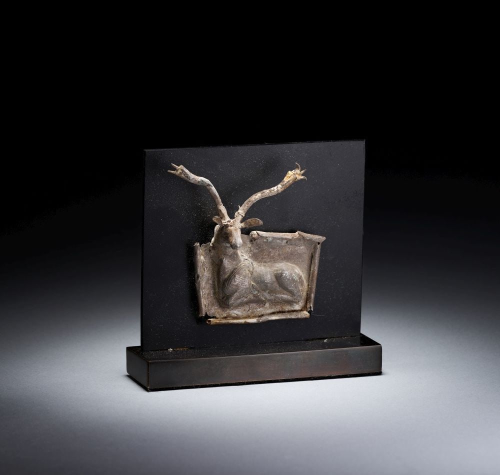 A SCYTHIAN SEATED STAG APPLIQUE, CIRCA 5TH CENTURY B.C.: A SCYTHIAN SEATED STAG APPLIQUE, CIRCA 5TH CENTURY B.C. A Scythian appliqué depicting a seated stag in high relief, shown recumbent with the legs folded beneath the body and the head turned for