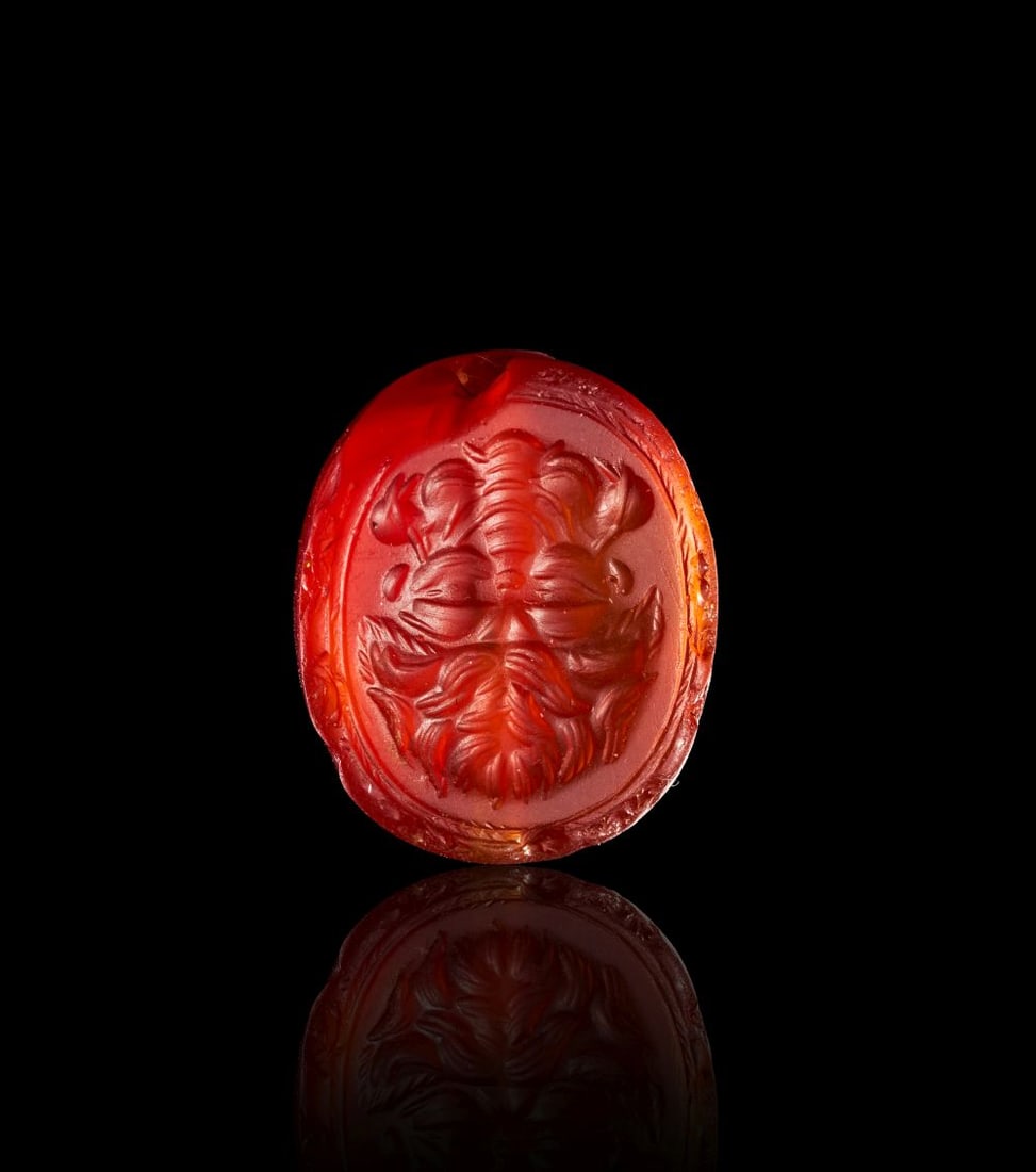 A GREEK CARNELIAN SCARABOID WITH A LION AND BES ARCHAIC PERIOD, CIRCA 580-520 B.C.: A GREEK CARNELIAN SCARABOID WITH A LION AND BES ARCHAIC PERIOD, CIRCA 580-520 B.C. Carved from translucent carnelian, this small scaraboid seal has a warm orange-red body with deeper red tones at the 