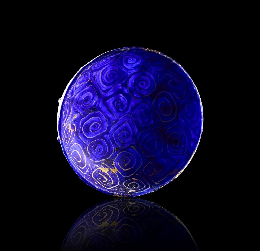A ROMAN DARK BLUE MARBLED GLASS BOWL CIRCA 1ST CENTURY A.D.: A ROMAN DARK BLUE MARBLED GLASS BOWL CIRCA 1ST CENTURY A.D. Cast in deep cobalt-blue glass, this shallow Roman bowl has a broad rounded body rising to a gently everted rim. Its compact, open form give