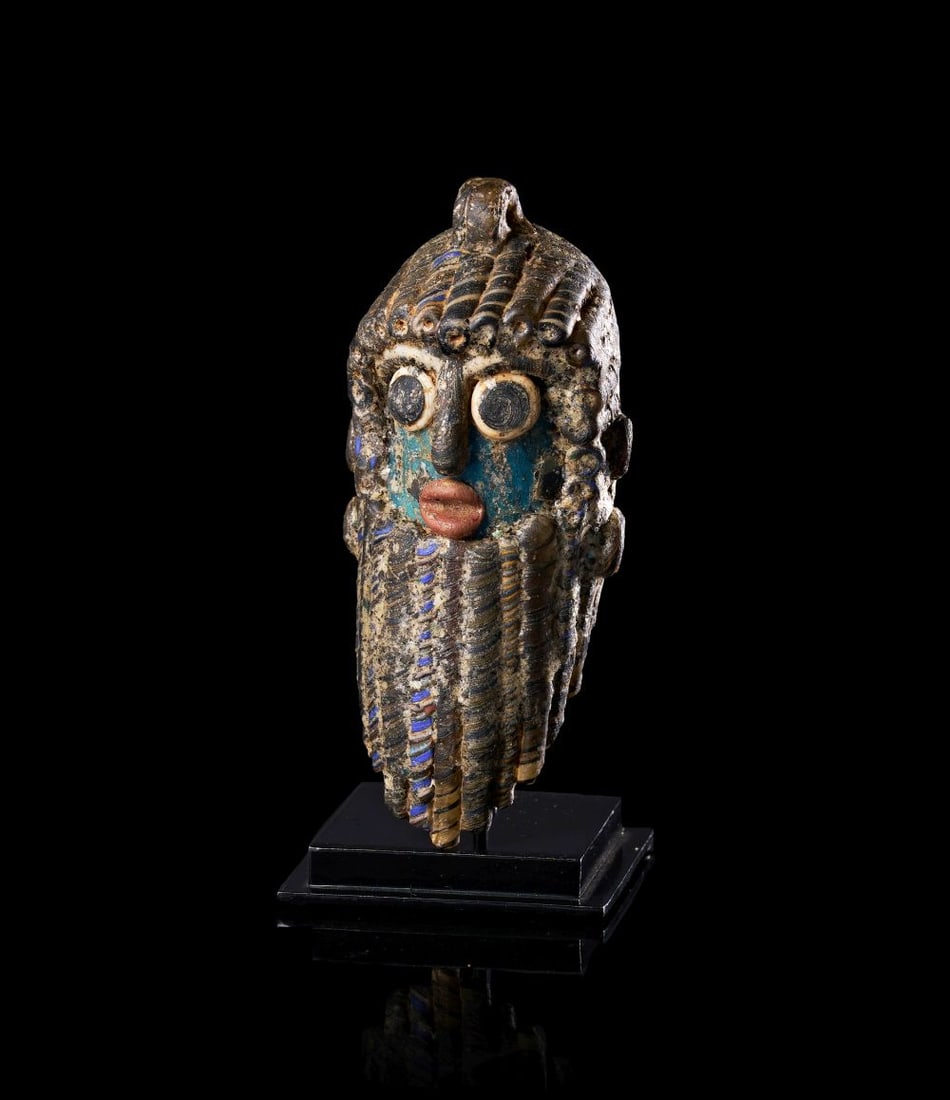 A PHOENICIAN GLASS BEARDED HEAD BEAD CIRCA 5TH-4TH CENTURY B.C.: A PHOENICIAN GLASS BEARDED HEAD BEAD CIRCA 5TH-4TH CENTURY B.C. A striking Phoenician glass bead formed as a miniature bearded head, modelled in the round with a powerful, mask-like presence. Th