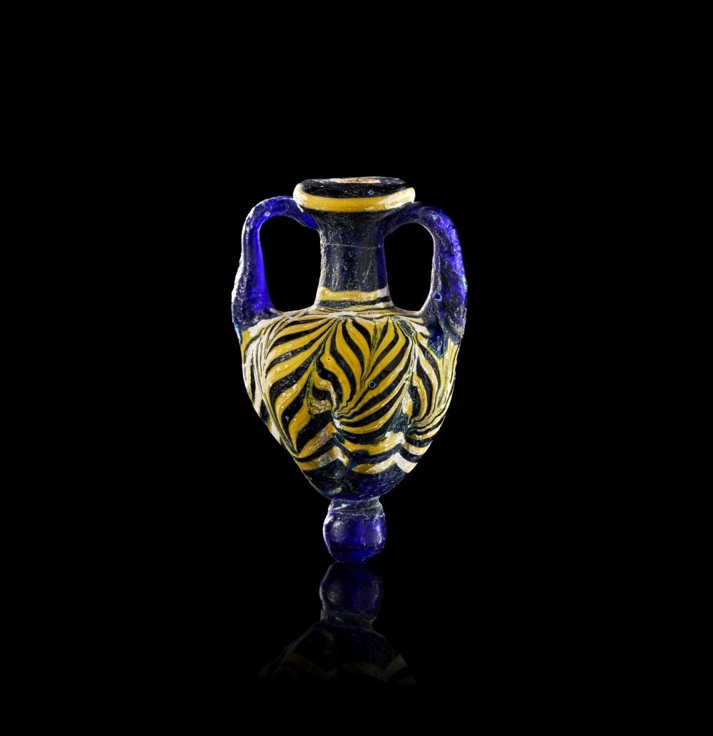 A PHOENICIAN GLASS AMPHORA, CIRCA 6TH-3RD CENTURY B.C.: A PHOENICIAN GLASS AMPHORA, CIRCA 6TH-3RD CENTURY B.C. The miniature amphora is formed in deep cobalt-blue glass, with a rounded ovoid body, narrow neck, everted rim and twin loop handles. Its compact