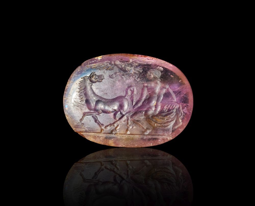 A ROMAN AMETHYST OF A SEATED MERCURY AND HORSE . CIRCA: 1ST CENTURY B.C.: A ROMAN AMETHYST OF A SEATED MERCURY AND HORSE . CIRCA: 1ST CENTURY B.C. Carved from pale purple amethyst, this oval intaglio presents a finely worked mythological scene within a compact horizontal fi