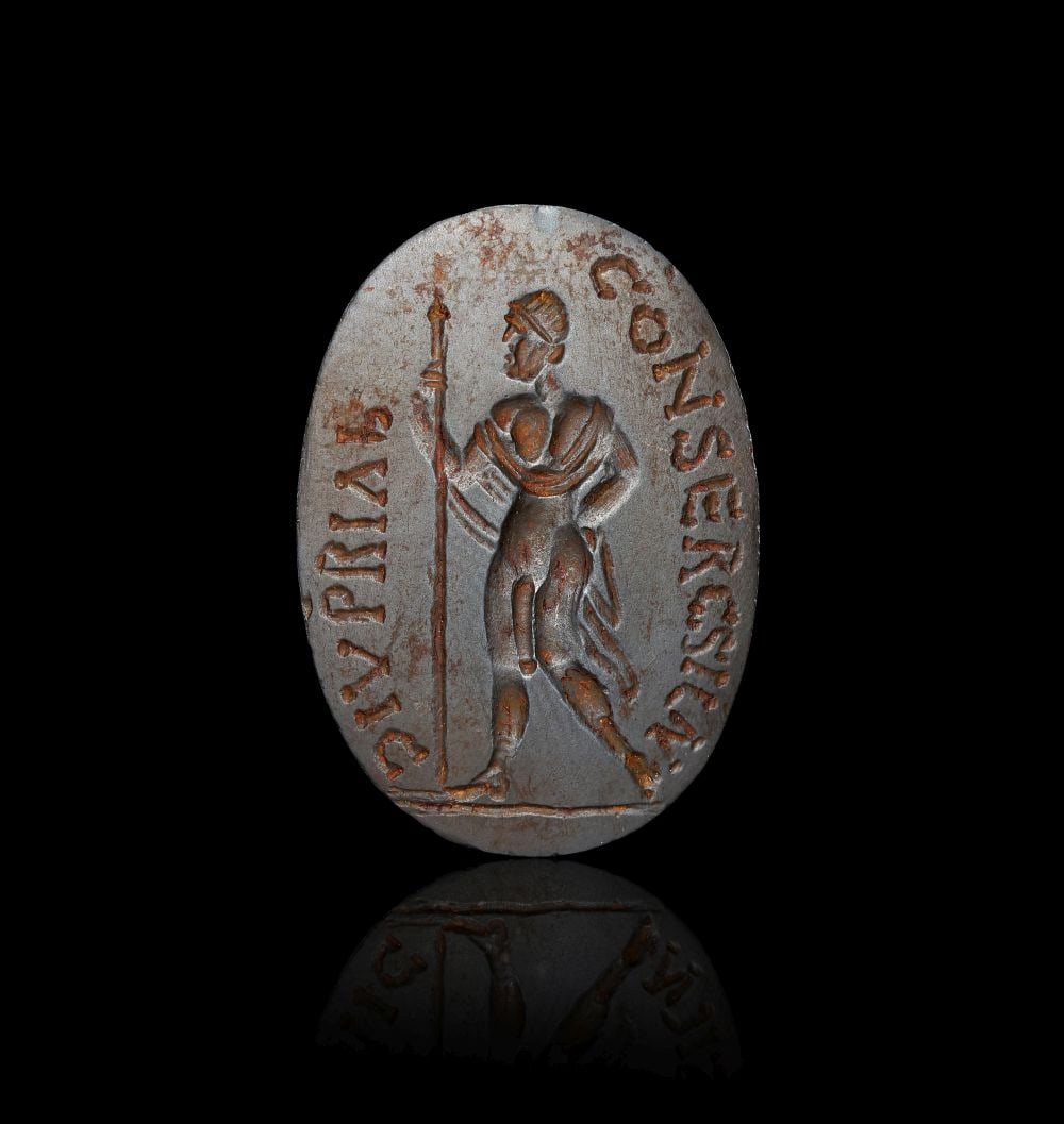 A ROMAN HEMATITE MAGICAL INTAGLIO WITH A STANDING HERO AND HOLDING A SPEARHEAD WITH INSCRIPTION ON R (1 of 2)