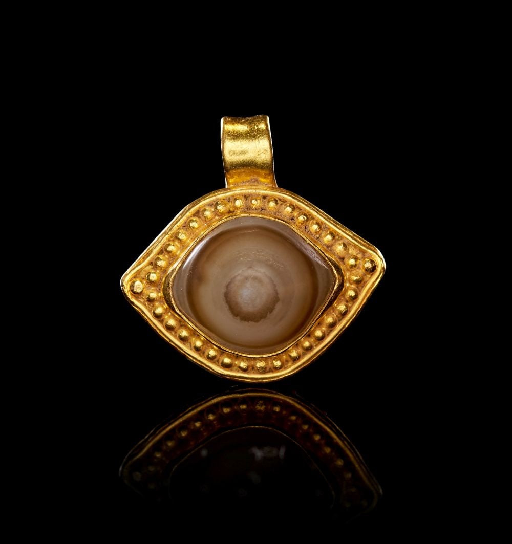 A ROMAN GOLD & AGATE "DZI" EYE BEAD, CIRCA 1ST-2ND CENTURY A.D.: A ROMAN GOLD & AGATE "DZI" EYE BEAD, CIRCA 1ST-2ND CENTURY A.D. Formed in gold and set with an agate eye bead, this Roman pendant is designed as a compact amuletic jewel. The body is shaped as a r