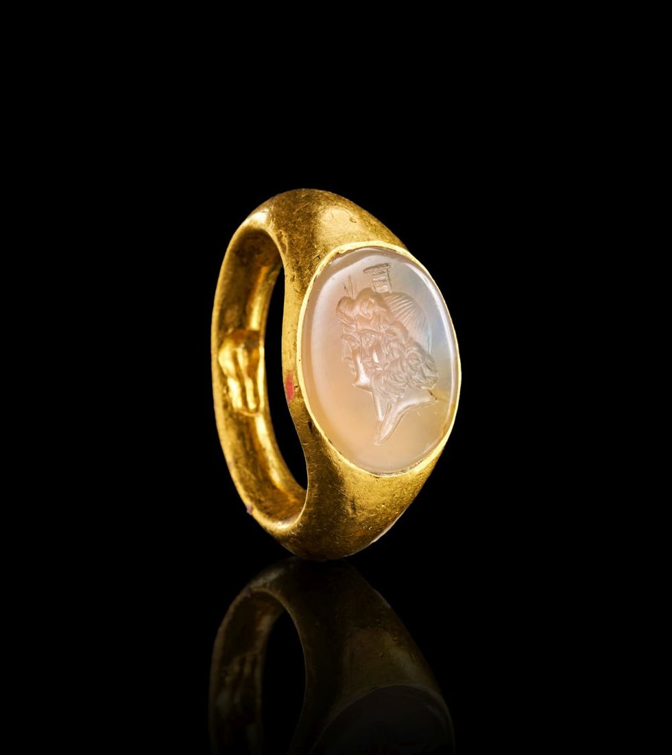 ROMAN GOLD RING WITH AGATE ENGRAVED CAPITA JUGATA STYLE PORTRAITS OF SERAPIS AND ISIS. CIRCA: 200-30: ROMAN GOLD RING WITH AGATE ENGRAVED CAPITA JUGATA STYLE PORTRAITS OF SERAPIS AND ISIS. CIRCA: 200-30 Formed in gold, this Roman finger ring is set with an oval agate intaglio engraved with paired prof