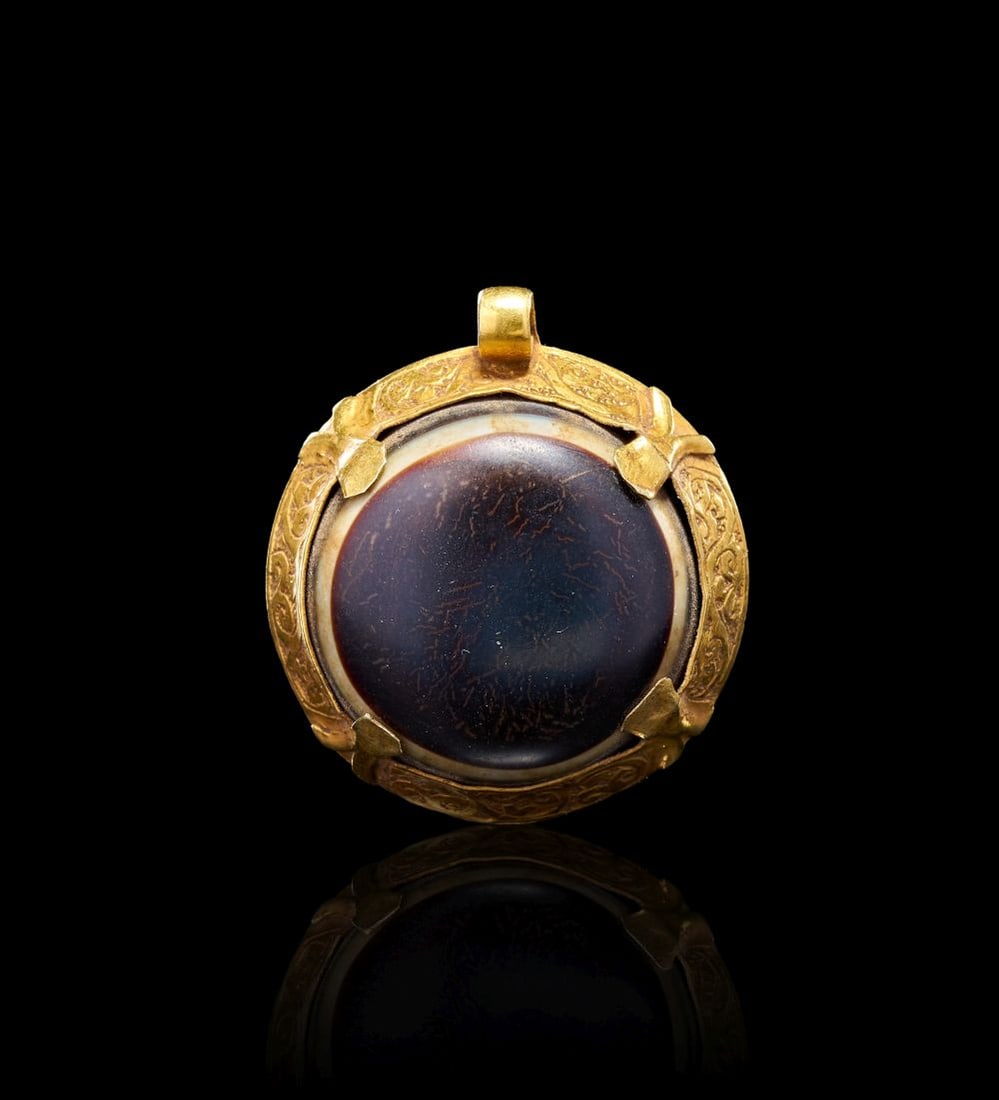 A RARE ROMAN AGATE "DZI" EYE BEAD, SET ON A HIGH KARAT GOLD MOUNT, 1ST-2ND CENTURY A.D.: A RARE ROMAN AGATE "DZI" EYE BEAD, SET ON A HIGH KARAT GOLD MOUNT, 1ST-2ND CENTURY A.D. Set in a high karat gold mount, this Roman pendant is centred by a large agate “Dzi” eye bead. The c