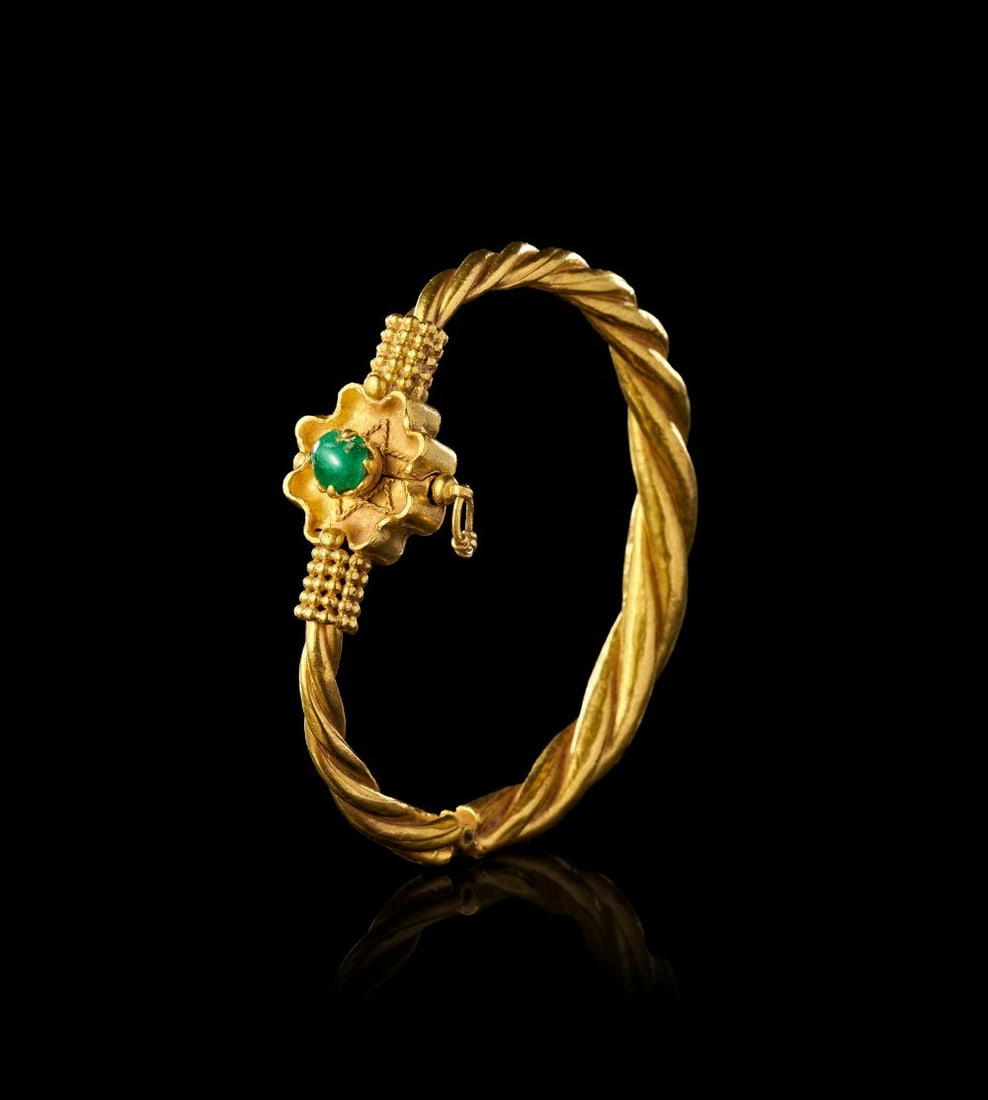 A FINE FATIMID GOLD & EMERALD BRACELET, EGYPT, 10TH CENTURY: A FINE FATIMID GOLD & EMERALD BRACELET, EGYPT, 10TH CENTURY Formed in gold, this Fatimid bracelet is designed as a twisted circular hoop, centred by a floral clasp set with a green emerald. The bo