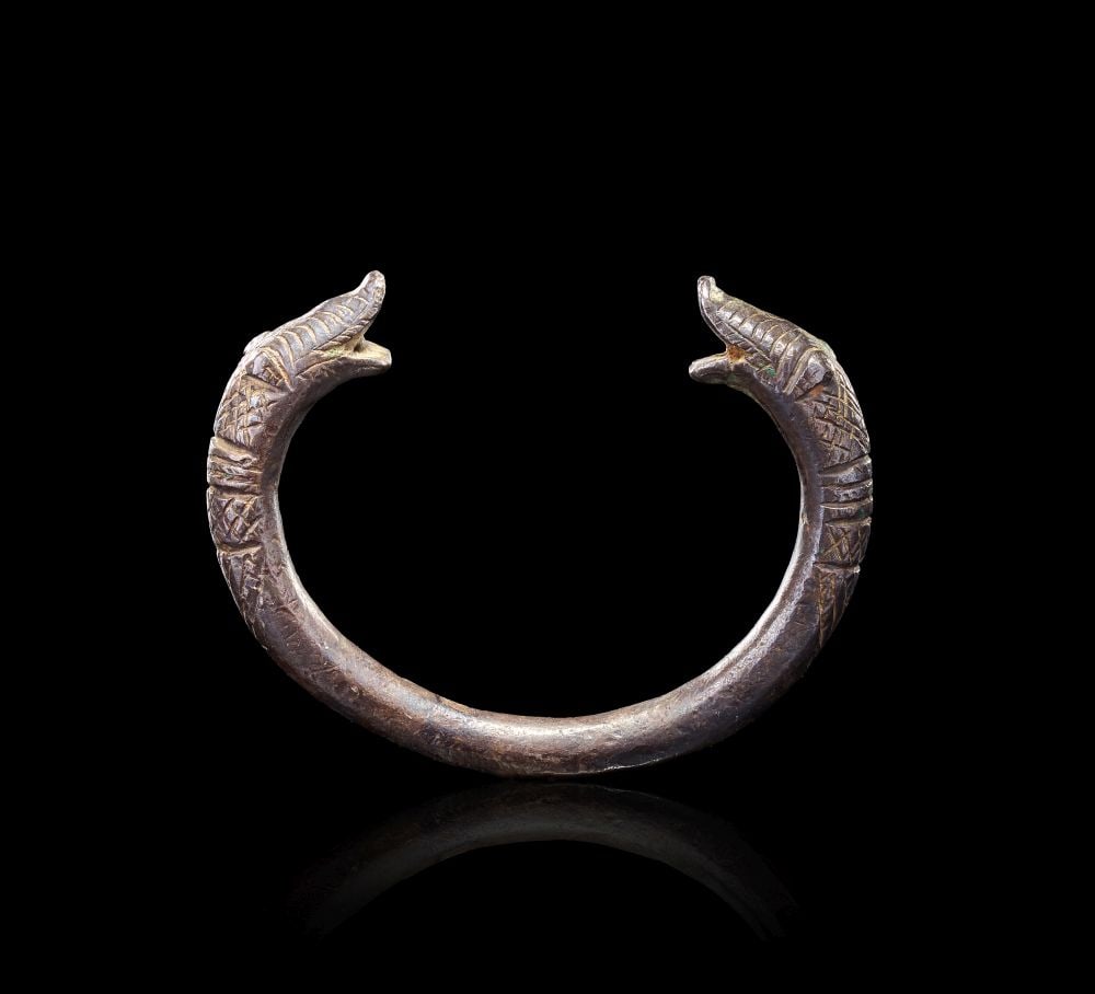 A SELJUK SILVER BRACELET PERSIA, 12TH CENTURY: A SELJUK SILVER BRACELET PERSIA, 12TH CENTURY Formed in silver, this Seljuk bracelet has an open circular hoop with opposing animal-head terminals. The broad curved body is substantial in scale, with 