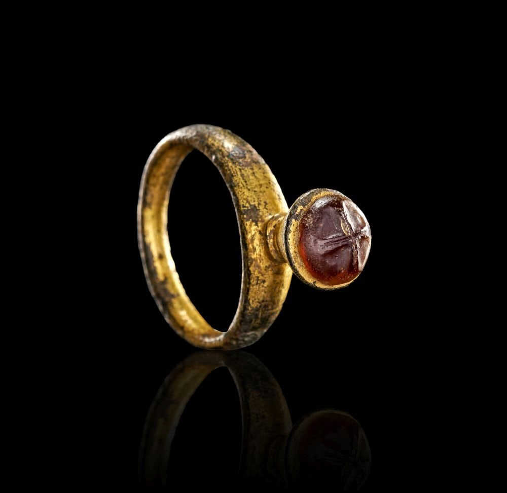 A BYZANTINE GILT BRONZE RING WITH AN AGATE IN THE FORM OF A CROSS, CIRCA 10TH-13TH CENTURY A.D.: A BYZANTINE GILT BRONZE RING WITH AN AGATE IN THE FORM OF A CROSS, CIRCA 10TH-13TH CENTURY A.D. Formed in gilt bronze, this Byzantine ring is set with a rounded red agate bezel engraved in the form of
