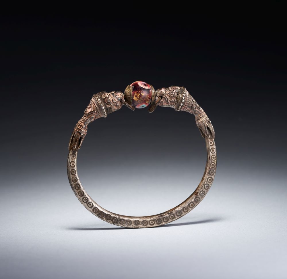 AN EAST GREEK SILVER LION-HEADED BRACELET CIRCA 4TH-3RD CENTURY B.C.: AN EAST GREEK SILVER LION-HEADED BRACELET CIRCA 4TH-3RD CENTURY B.C. Formed in silver, this East Greek bracelet has an open circular hoop terminating in confronting lion heads. The body is slender and