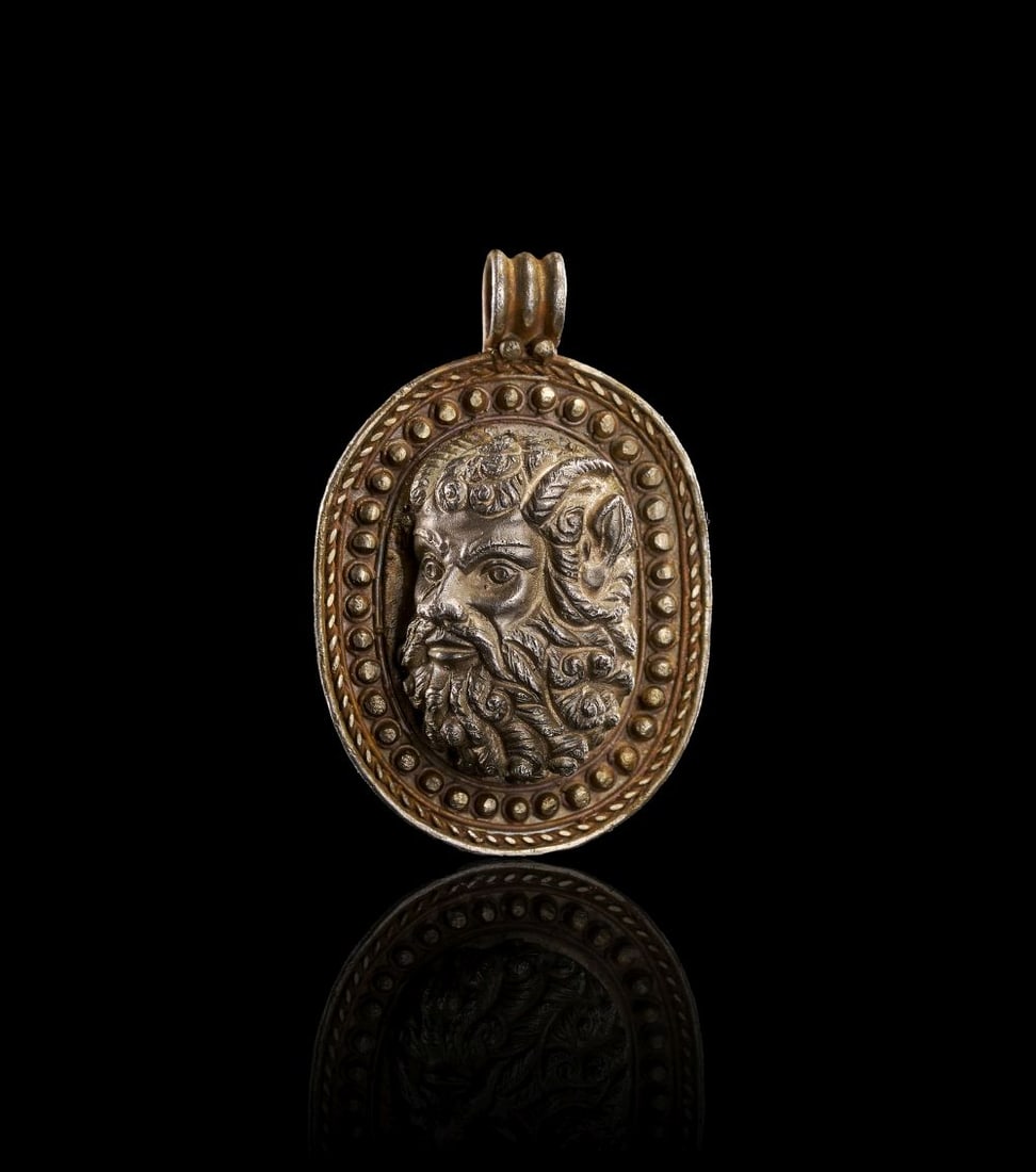 A GREEK SILVER PENDANT DEPICTING A SATYR, CIRCA 3RD CENTURY A.D.: A GREEK SILVER PENDANT DEPICTING A SATYR, CIRCA 3RD CENTURY A.D. Formed in silver, this pendant is centred by a relief bust of a satyr within an oval frame. The face is strongly modelled, with deeply 