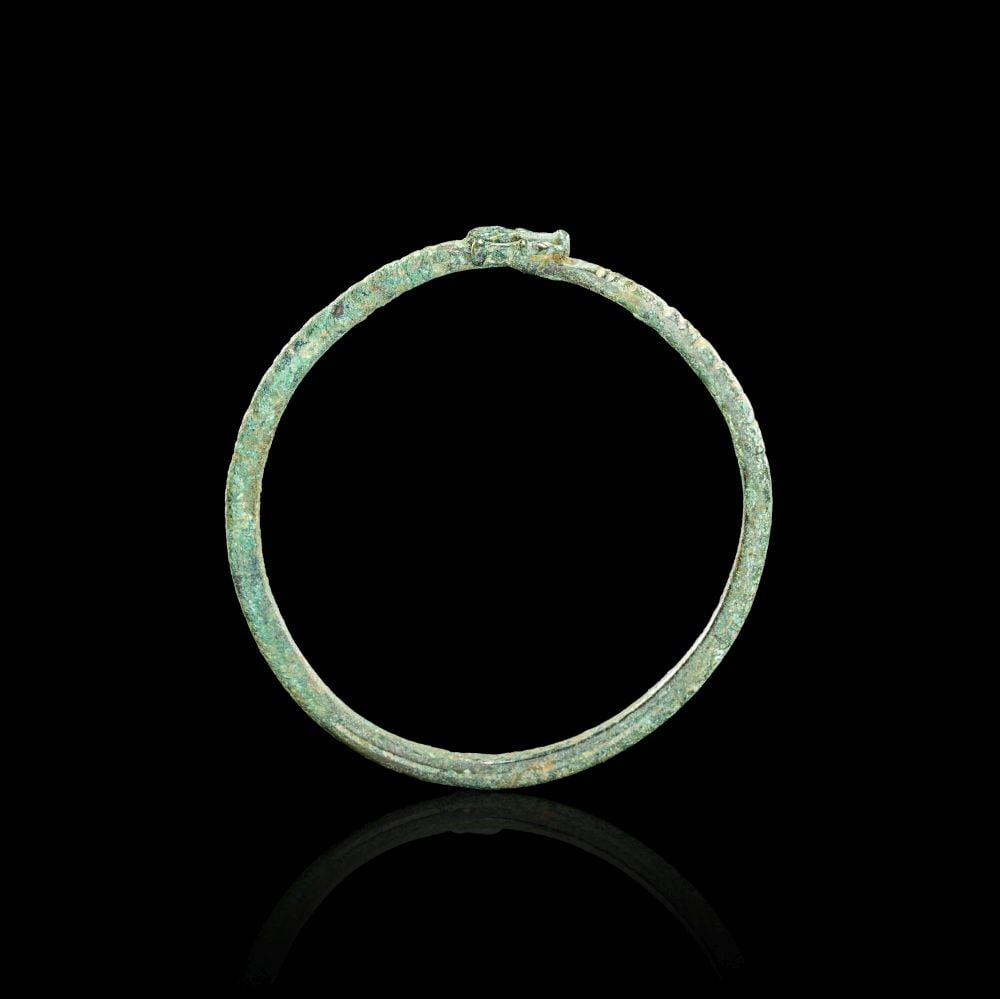 A CELTIC BRONZE TORQUE CIRCA 4TH CENTURY B.C.: A CELTIC BRONZE TORQUE CIRCA 4TH CENTURY B.C. Formed in bronze, this Celtic torque has a circular hoop with a compact terminal element at the top. The surface is covered with a green patina, giving th