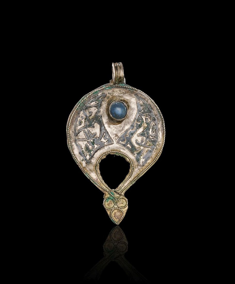 A SELJUK NIELLOED SILVER GEM SET AMULET, IRAN, 12TH OR 13TH CENTURY: A SELJUK NIELLOED SILVER GEM SET AMULET, IRAN, 12TH OR 13TH CENTURY Formed in silver, this Seljuk amulet has a rounded pear-shaped body with an open lower section and a suspension loop above. The surf