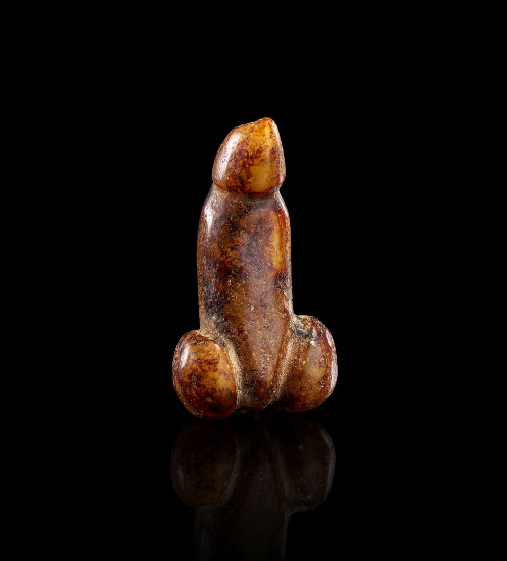 A GREEK AGATE PHALLUS AMULET, CIRCA 3RD CENTURY A.D.: A GREEK AGATE PHALLUS AMULET, CIRCA 3RD CENTURY A.D. Carved from warm honey-brown agate with darker reddish and umber inclusions, this compact amulet is formed as a phallus with rounded testicular bas