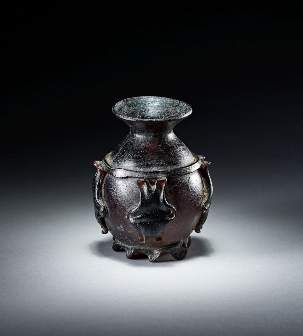 AN UMAYYAD OR EARLY ABBASID GLASS VASE WEST MEDITERRANEAN, 8TH/9TH CENTURY: AN UMAYYAD OR EARLY ABBASID GLASS VASE WEST MEDITERRANEAN, 8TH/9TH CENTURY Of deep aubergine-brown glass, the vase is blown with a globular body, short waisted neck and broad flaring mouth. The surfac
