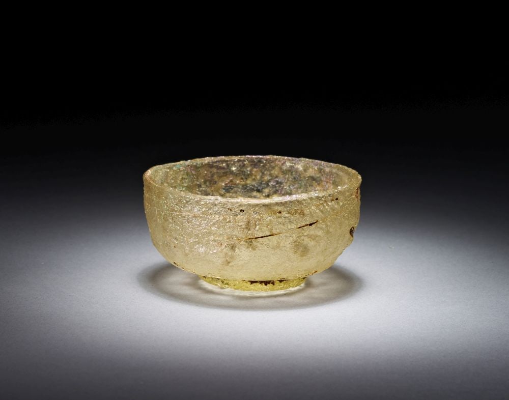 A ROMAN GLASS BOWL, CIRCA 1ST-2ND CENTURY A.D.: A ROMAN GLASS BOWL, CIRCA 1ST-2ND CENTURY A.D. Of pale yellowish glass, the bowl is blown with a rounded hemispherical body, a slightly thickened rim and a small circular foot. The surface has acquire