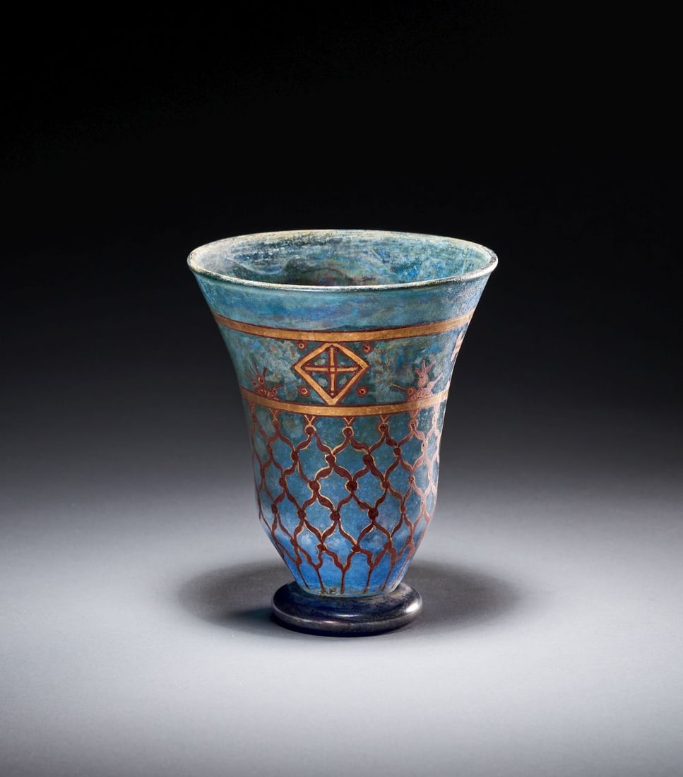 A LUSTRE DECORATED GLASS CUP: A LUSTRE DECORATED GLASS CUP Of blue glass, the cup is of flaring conical form, rising from a dark circular foot to a broad, slightly everted rim. The surface has an iridescent weathering which soften