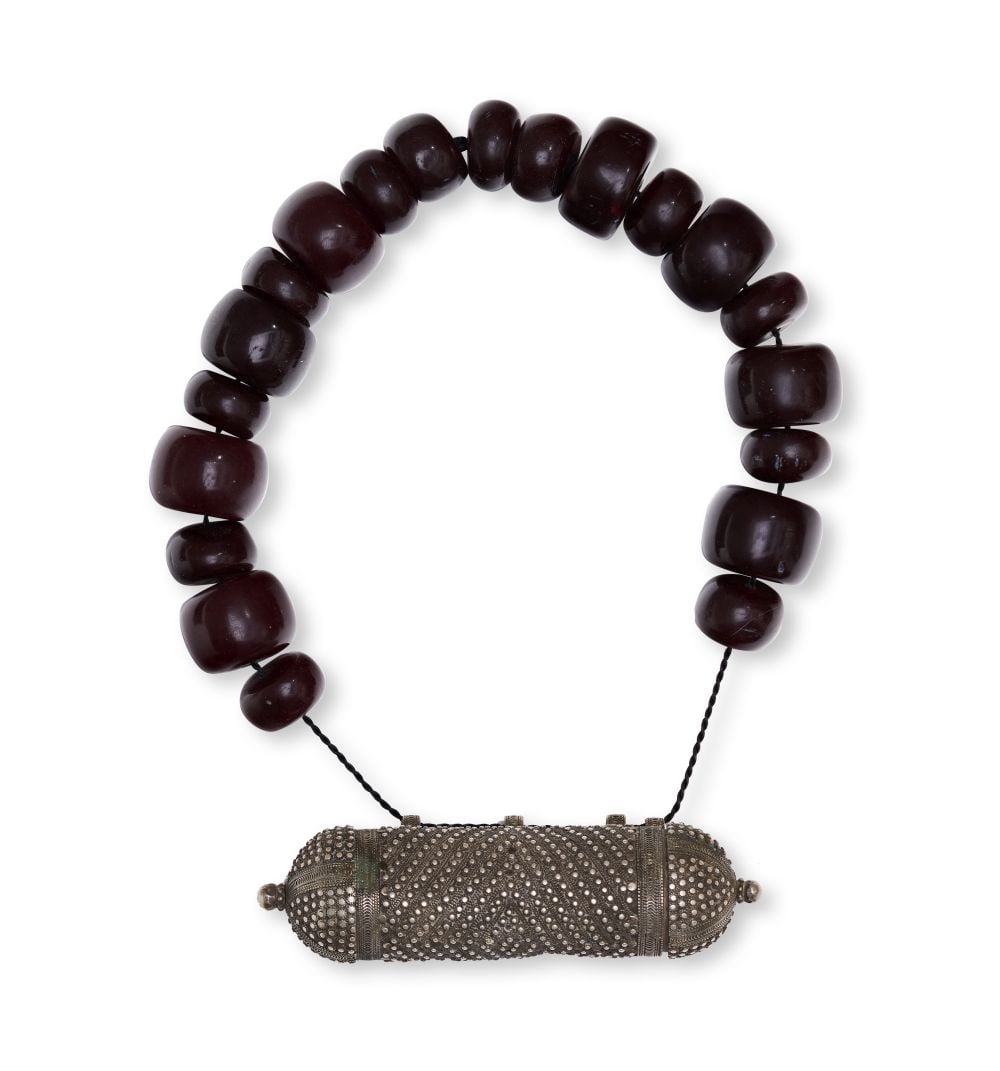 A CENTRAL ASIAN OR TRIBAL CHERRY AMBER & SILVER NECKLACE, 20TH CENTURY: A CENTRAL ASIAN OR TRIBAL CHERRY AMBER & SILVER NECKLACE, 20TH CENTURY Composed of dark cherry amber beads and a silver pendant, this necklace is notable for the contrast between the deep, polishe