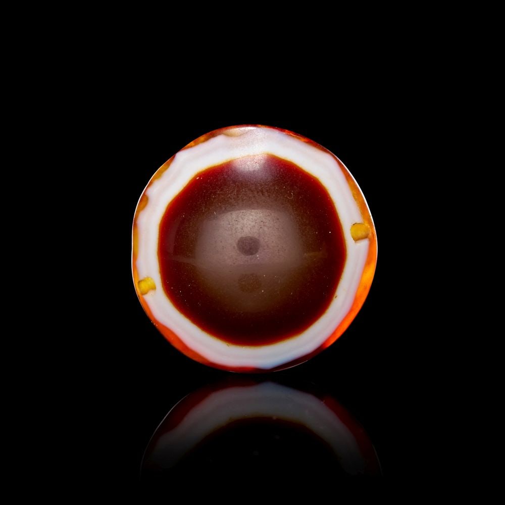 AN AGATE "DZI" EYE BEAD, 1ST-2ND CENTURY A.D. OR LATER: AN AGATE "DZI" EYE BEAD, 1ST-2ND CENTURY A.D. OR LATER Formed from polished agate, this circular bead presents a compact and highly concentrated image of colour and pattern. The stone is worked into a
