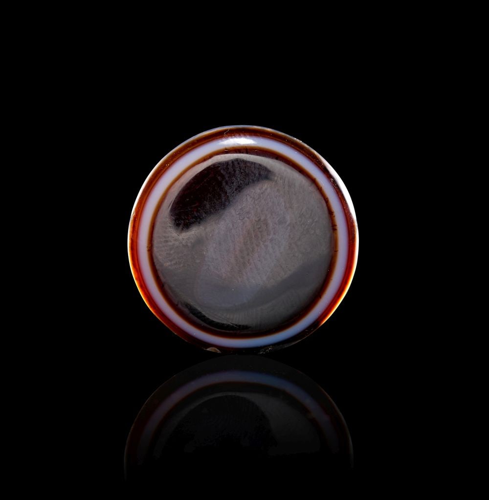 AN AGATE "DZI" EYE BEAD, 1ST-2ND CENTURY A.D. OR LATER: AN AGATE "DZI" EYE BEAD, 1ST-2ND CENTURY A.D. OR LATER Carved and polished from agate, this compact circular bead has a quiet, concentrated presence. Its rounded disc form is defined by a softly trans