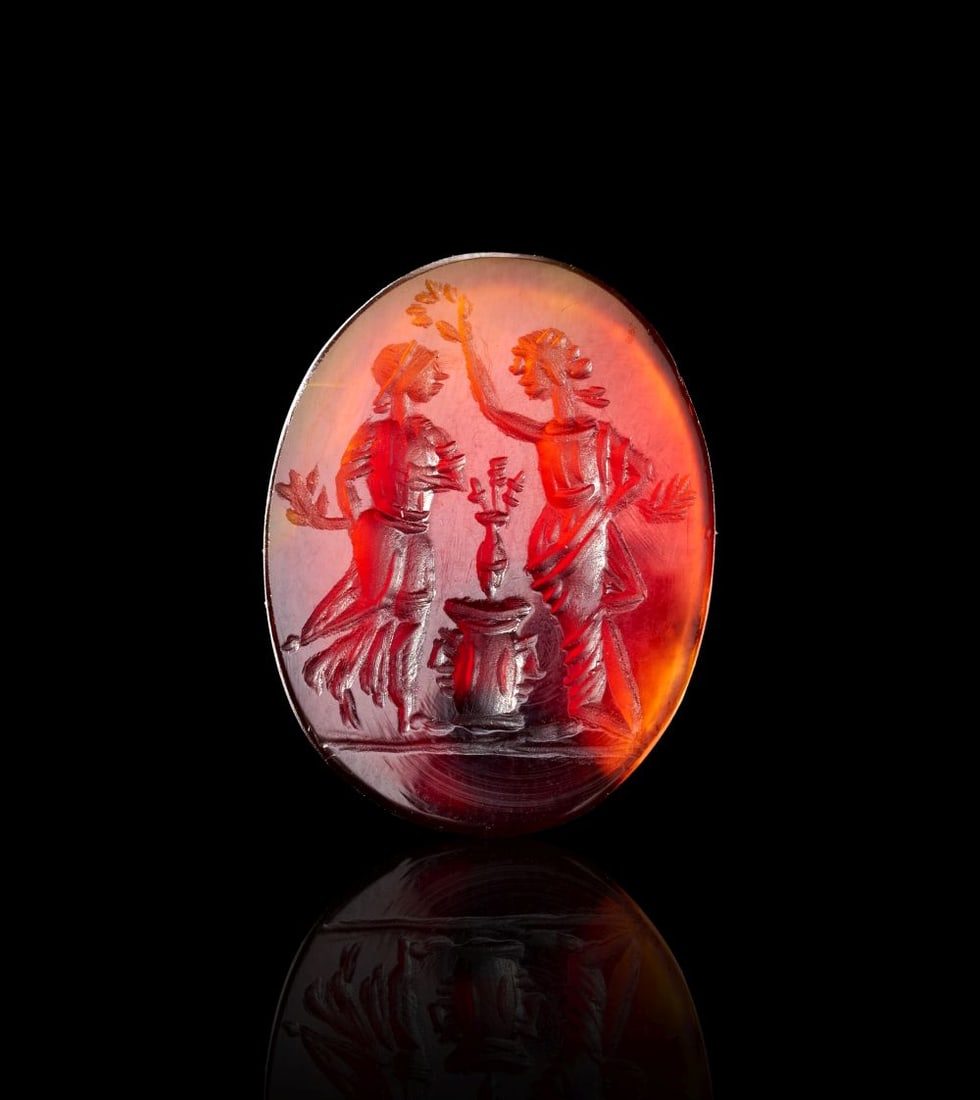 A GREEK INTAGLIO OF TWO MAIDENS, CIRCA 3RD CENTURY A.D. OR LATER: A GREEK INTAGLIO OF TWO MAIDENS, CIRCA 3RD CENTURY A.D. OR LATER Carved in deep red carnelian, this oval intaglio presents a compact figural scene within a smoothly polished gem surface. The stone is 