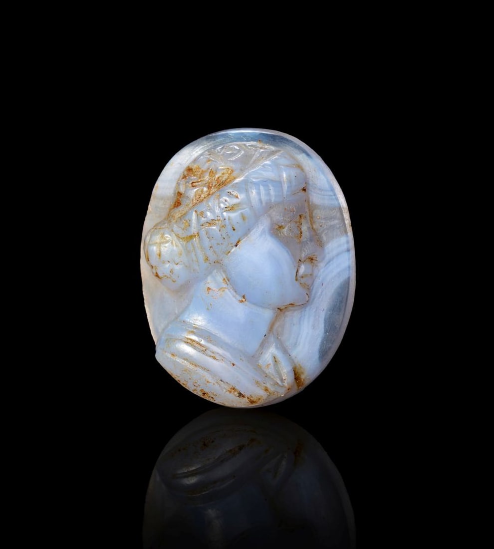 PTOLEMAIC BLUE BANDED CHALCEDONY CAMEO OF A BUST OF THE QUEEN ARSINOE, CIRCA 2ND CENTURY B.C.: PTOLEMAIC BLUE BANDED CHALCEDONY CAMEO OF A BUST OF THE QUEEN ARSINOE, CIRCA 2ND CENTURY B.C. Carved from blue banded chalcedony, this oval cameo presents the bust of Queen Arsinoe in profile, the pal