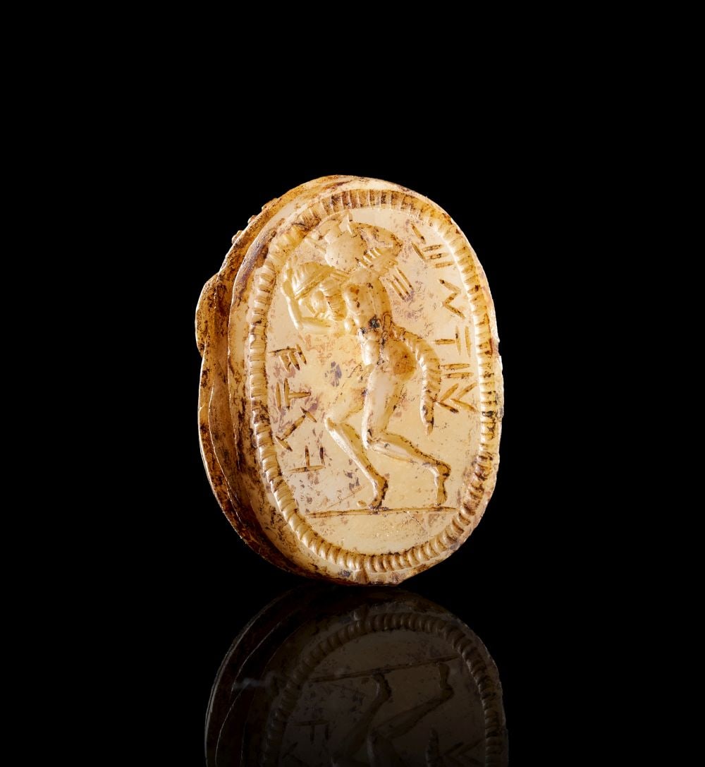 AN INSCRIBED SCARAB DEPICTING A FAUN WITH AN AMPHORA, CIRCA LATE 4TH-EARLY 3RD CENTURY B.C.: AN INSCRIBED SCARAB DEPICTING A FAUN WITH AN AMPHORA, CIRCA LATE 4TH-EARLY 3RD CENTURY B.C. Carved from a pale, honey-coloured hardstone, this scarab is worked in a compact oval form, its upper surfac