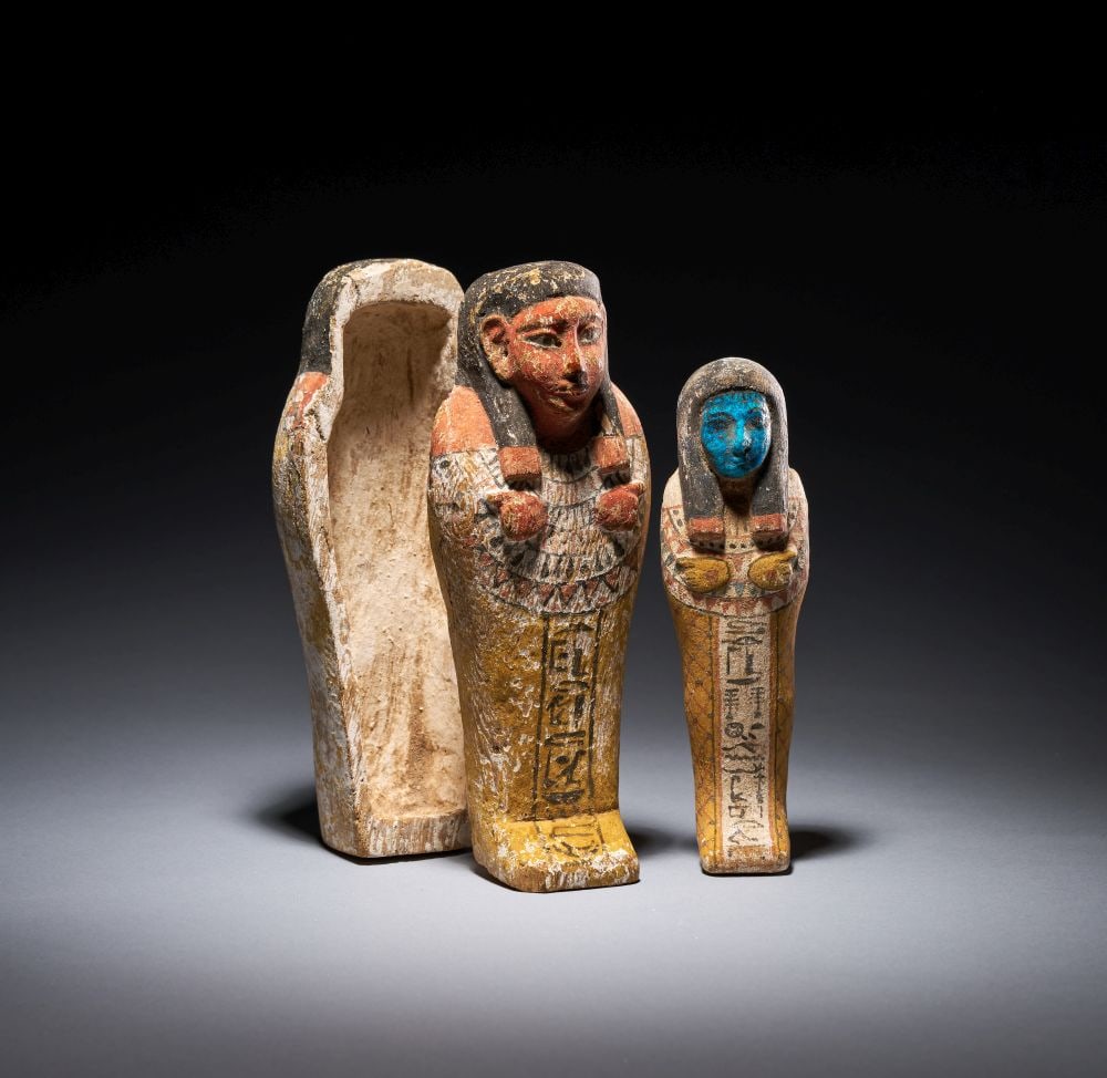 AN EGYPTIAN POLYCHROME PAINTED WOODEN SHABTI: AN EGYPTIAN POLYCHROME PAINTED WOODEN SHABTI Carved in wood and retaining extensive polychrome decoration, this shabti presents the deceased in mummiform guise, the body tapering towards a small integ