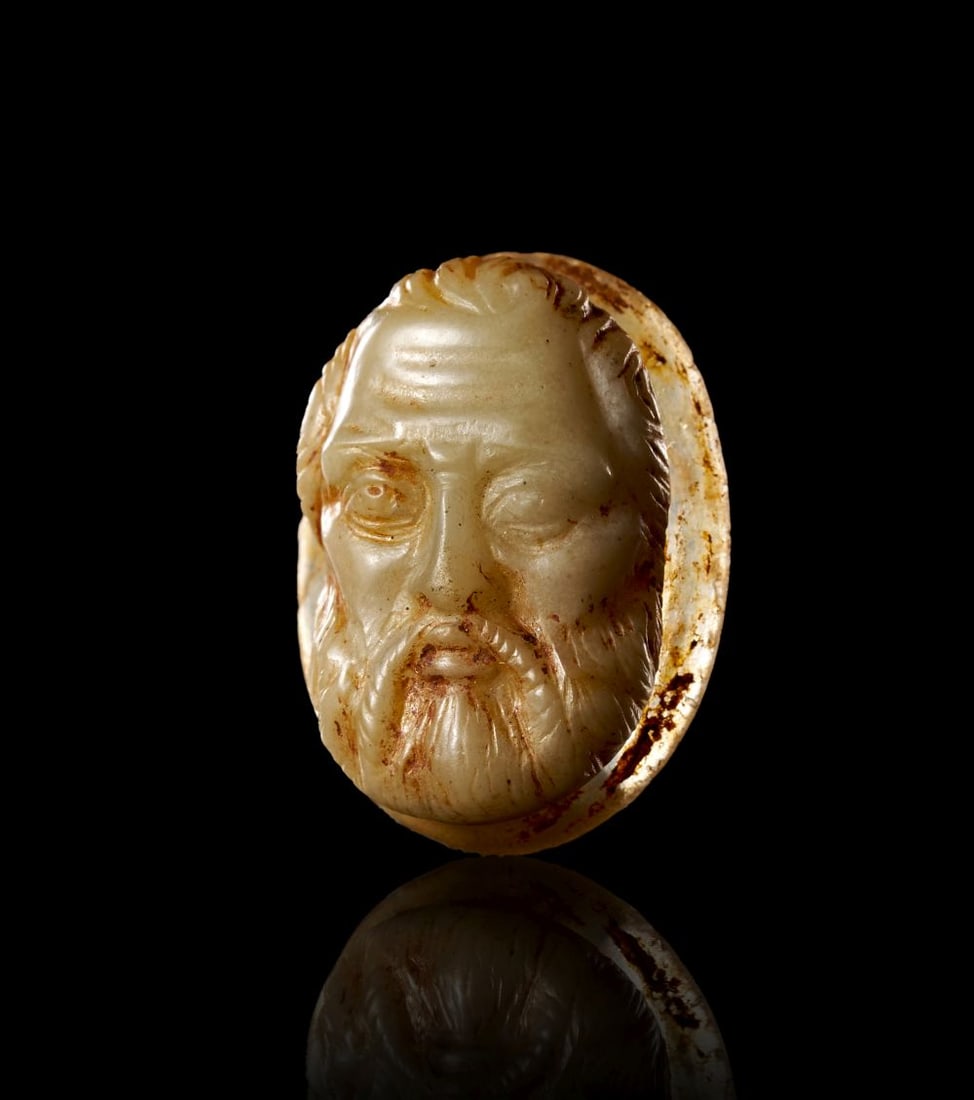 A ROMAN AGATE CAMEO OF BEARDED MAN OR THEATRICAL MASK: A ROMAN AGATE CAMEO OF BEARDED MAN OR THEATRICAL MASK The small oval cameo is carved from agate of pale cream and honey tones, its layered stone used to give definition to a frontal bearded head. The 
