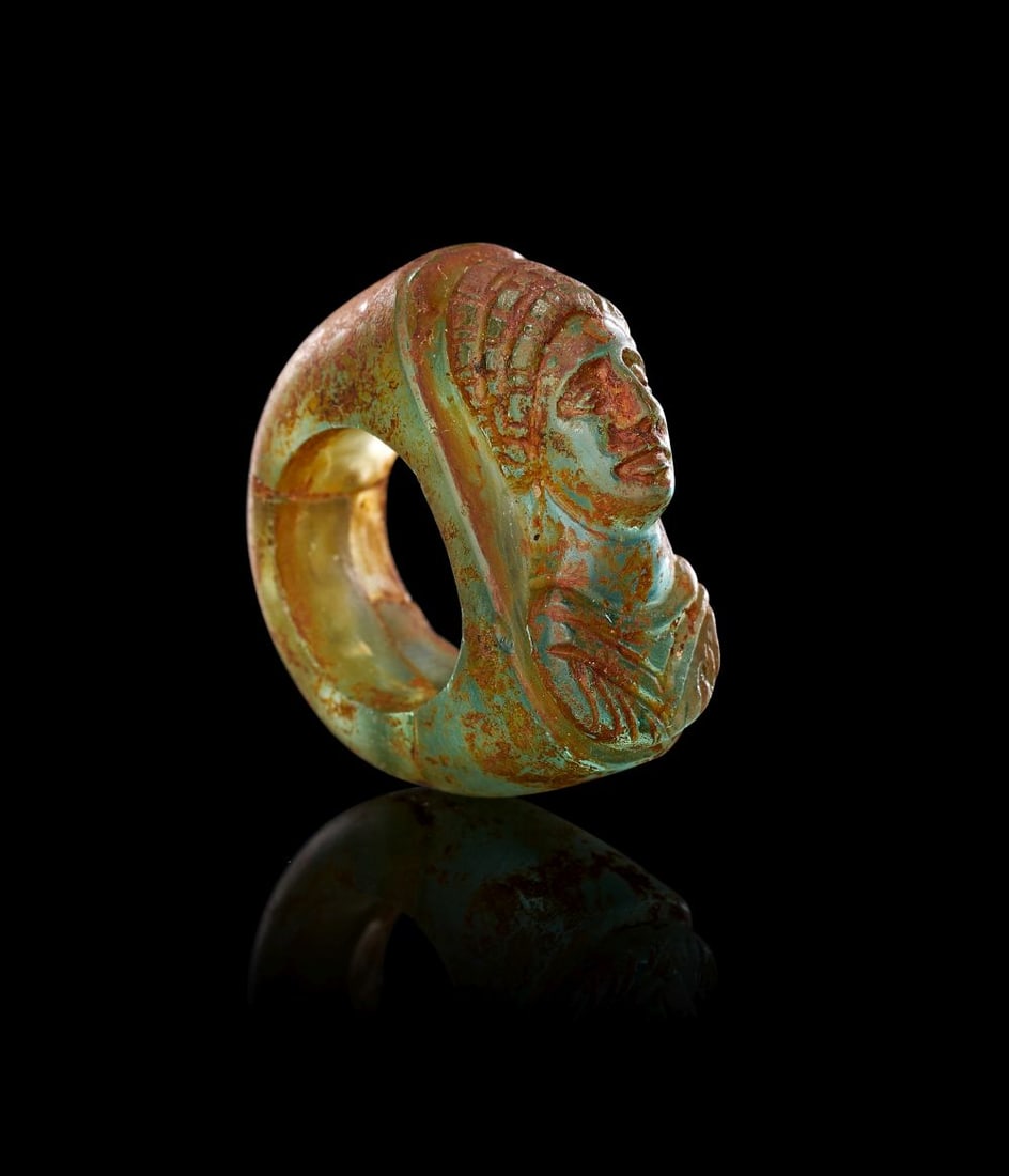 A ROMAN GREEN GLASS RING WITH BUST OF AGRIPPINA THE YOUNGER IN PORTRAIT, CIRCA 1ST-2ND CENTURY A.D.: A ROMAN GREEN GLASS RING WITH BUST OF AGRIPPINA THE YOUNGER IN PORTRAIT, CIRCA 1ST-2ND CENTURY A.D. The ring is formed in translucent green glass, the broad hoop rising to an integral oval bezel carve