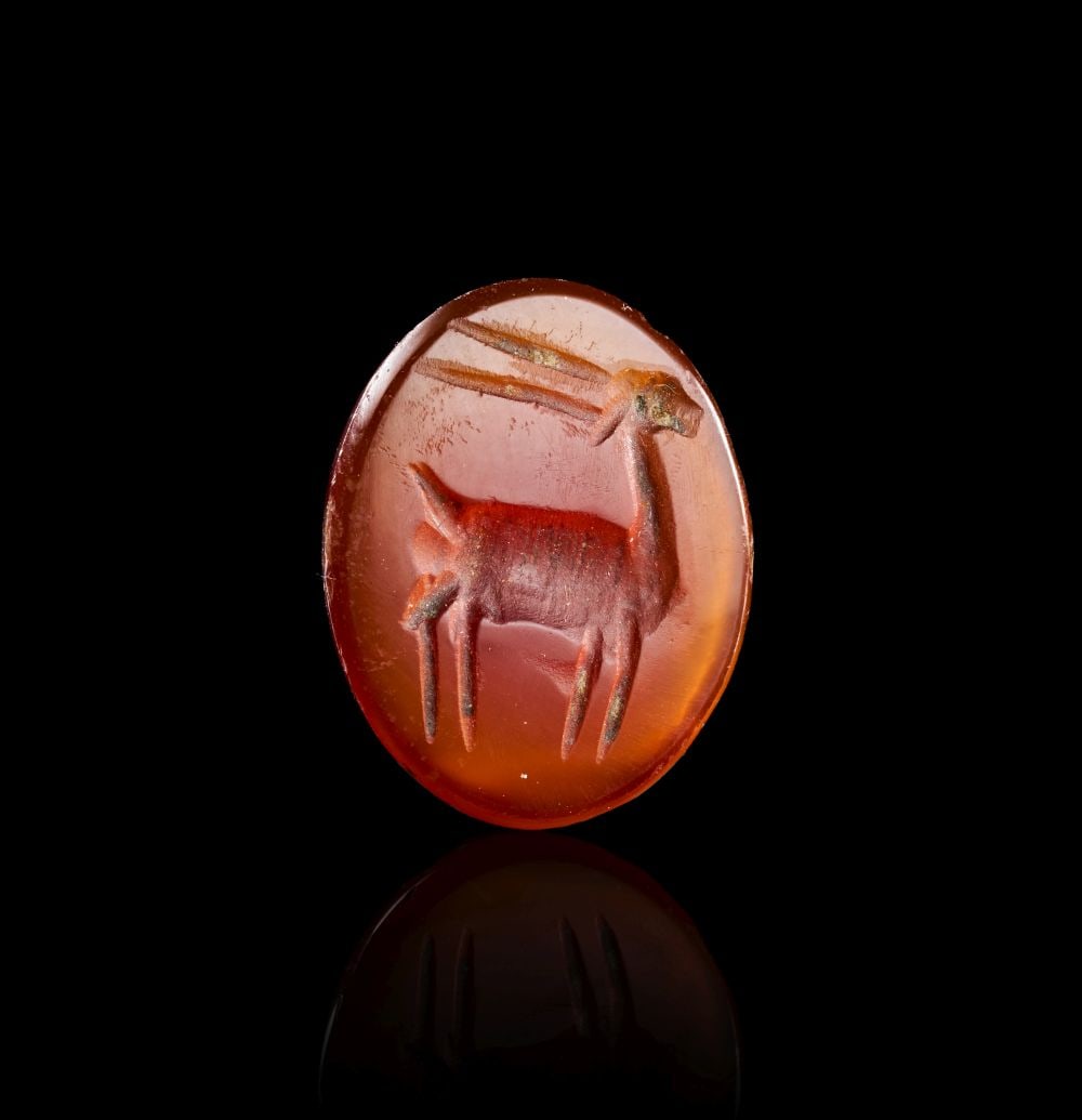 AN EASTERN AGATE INTAGLIO ENGRAVED DEPICTING A STANDING IBEX, CIRCA 1ST-2ND CENTURY A.D.: AN EASTERN AGATE INTAGLIO ENGRAVED DEPICTING A STANDING IBEX, CIRCA 1ST-2ND CENTURY A.D. The oval intaglio is carved from warm orange-red agate, the translucent body of the stone giving depth to the e