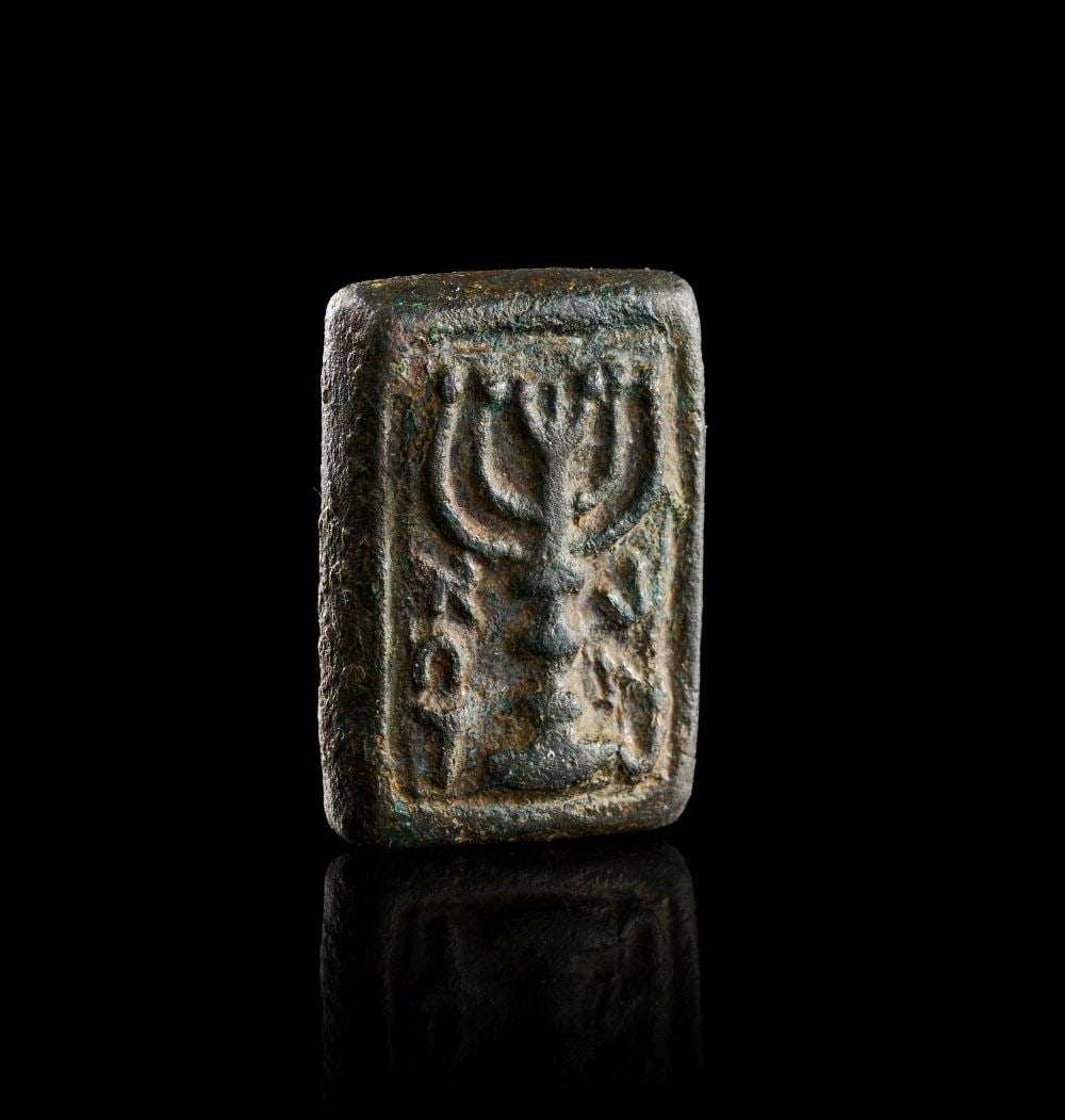 A WESTERN ASIATIC BRONZE STAMP SEAL WITH MENORAH AND HORNED BULL ON REVERSE, CIRCA 7TH CENTURY B.C.: A WESTERN ASIATIC BRONZE STAMP SEAL WITH MENORAH AND HORNED BULL ON REVERSE, CIRCA 7TH CENTURY B.C. A small rectangular bronze stamp seal, the surfaces heavily patinated with dark green, brown and pal