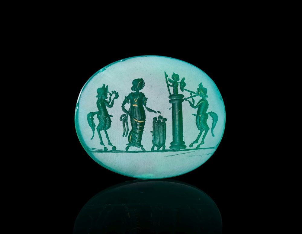 AN INTAGLIO DEPICTING A MYTHICAL SCENE: AN INTAGLIO DEPICTING A MYTHICAL SCENE An oval turquoise-green intaglio engraved with a finely detailed mythical scene. At the centre stands a draped female figure beside a small altar or incense burn