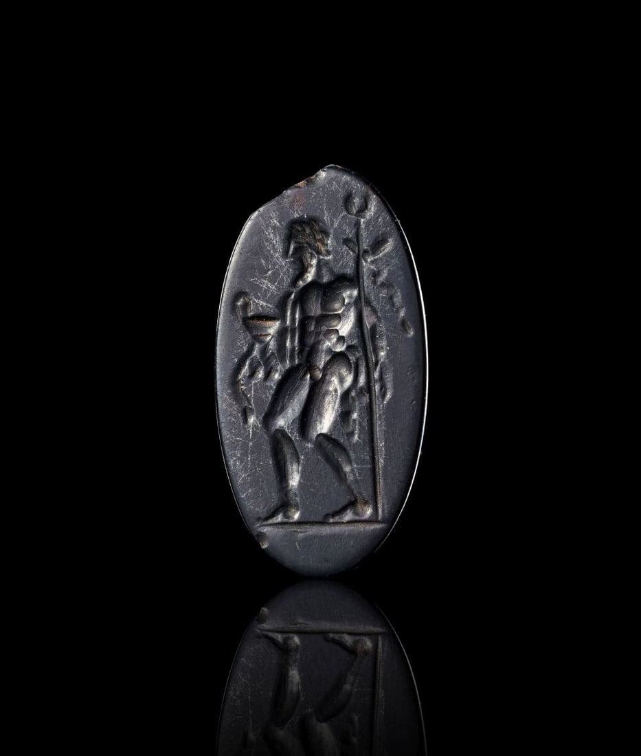 A GREEK JASPER INGALIO OF AN ATHLETE HOLDING A WINE CUP & SCEPTRE, 3RD CENTURY A.D. OR LATER: A GREEK JASPER INGALIO OF AN ATHLETE HOLDING A WINE CUP & SCEPTRE, 3RD CENTURY A.D. OR LATER The oval intaglio is cut from dark jasper, its polished surface providing a clear ground for the finely