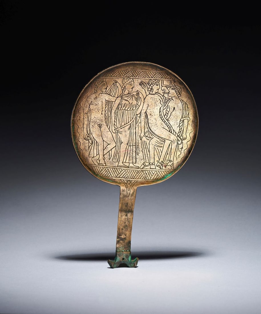 AN ETRUSCAN STYLE BRONZE MIRROR: AN ETRUSCAN STYLE BRONZE MIRROR The bronze mirror is formed with a circular disc and a slender integral handle, the surface engraved with a finely organised figural scene. Its broad, shallow roundel g