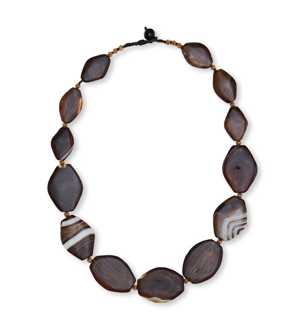 A BANDED AGATE NECKLACE, IN THE MANNER OF ELAMITE: A BANDED AGATE NECKLACE, IN THE MANNER OF ELAMITE Composed of large graduated banded agate beads, this necklace is arranged in a balanced sequence of flattened, irregular oval and faceted forms. The s