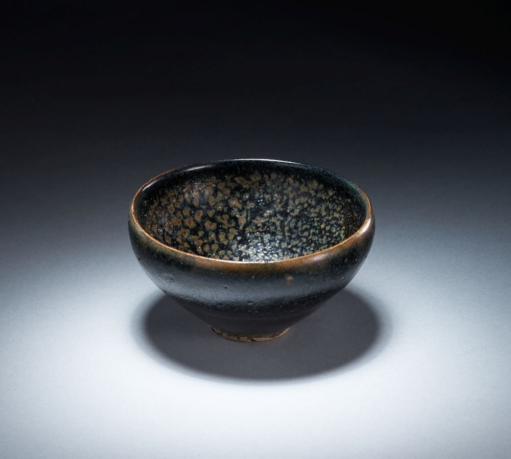 A SMALL 'OIL SPOT' TEA BOWL JIN DYNASTY (1115-1234): A SMALL 'OIL SPOT' TEA BOWL JIN DYNASTY (1115-1234) The tea bowl is of small, rounded form, rising from a short foot to a gently incurved rim. It is covered in a dark black-brown glaze, thickly pooled
