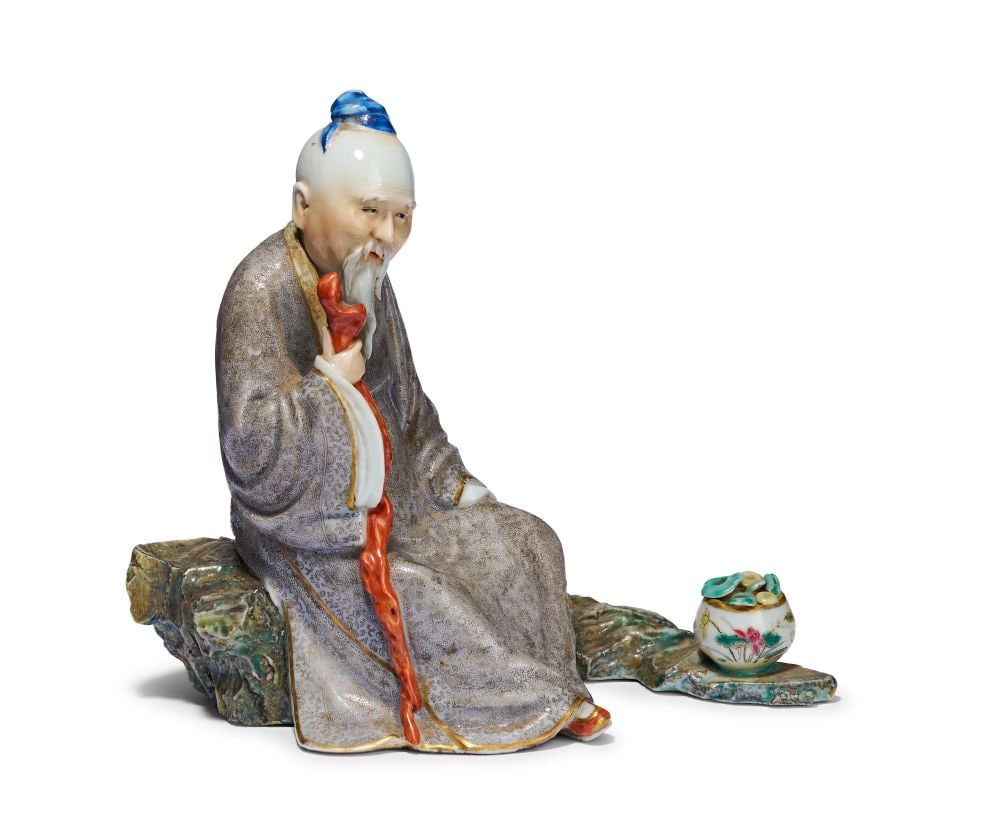A FAMILLE ROSE FIGURE OF A DAOIST PRIEST, REPUBLICAN PERIOD: A FAMILLE ROSE FIGURE OF A DAOIST PRIEST, REPUBLICAN PERIOD Height: 17cm Seated upon a naturalistically modelled rockwork base washed in green, blue and ochre glazes, the elderly figure leans slightly